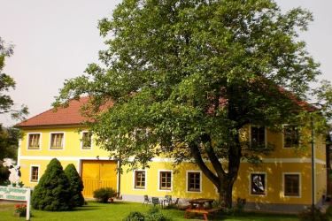 Žltá budova s červenou strechou a veľkým stromom v popredí.