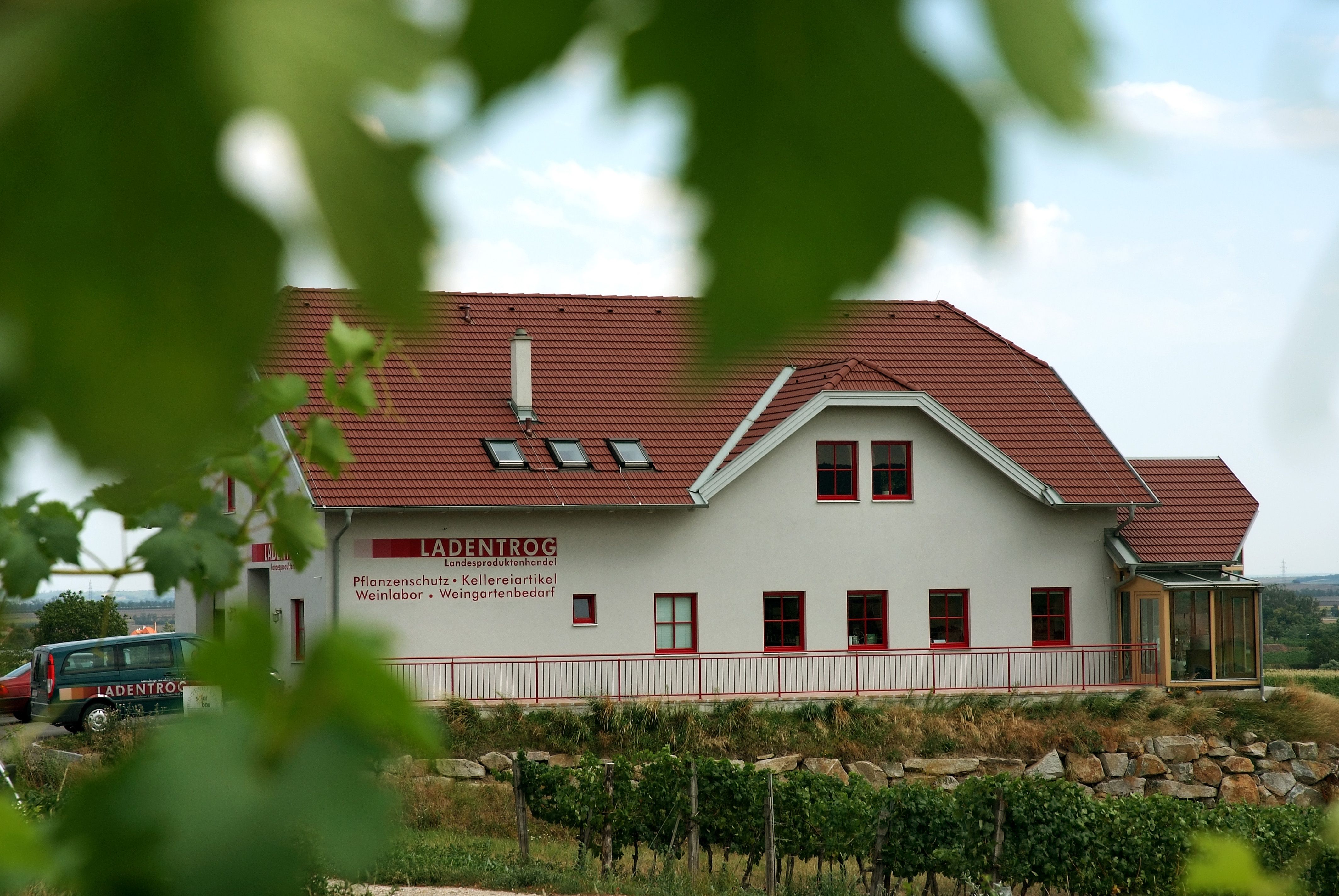 Budova s červenou strechou a nápisom "LADENTROG" vo vidieckom prostredí.
