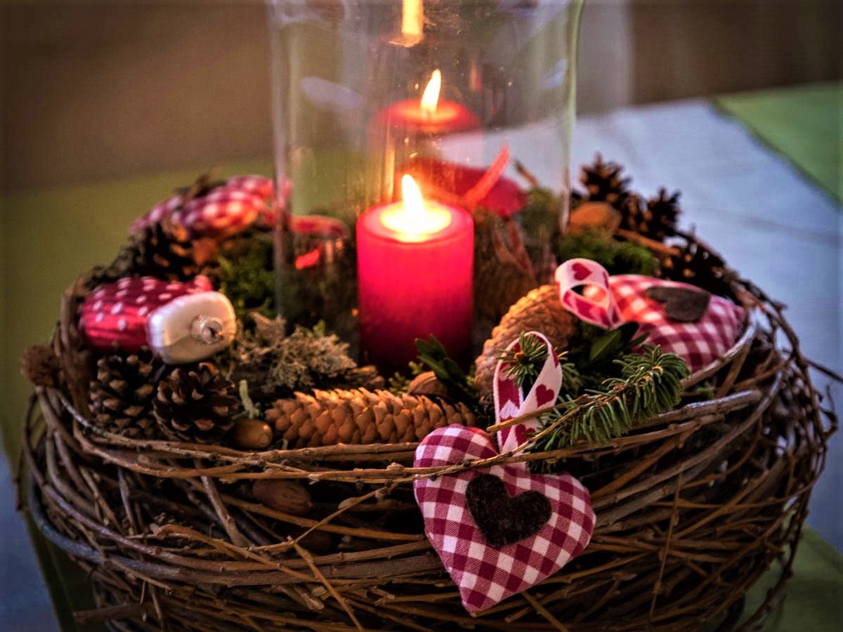 Adventný veniec s horiacou červenou sviečkou, borovicovými šiškami a červeno-bielymi šachovnicovými látkovými srdiečkami.