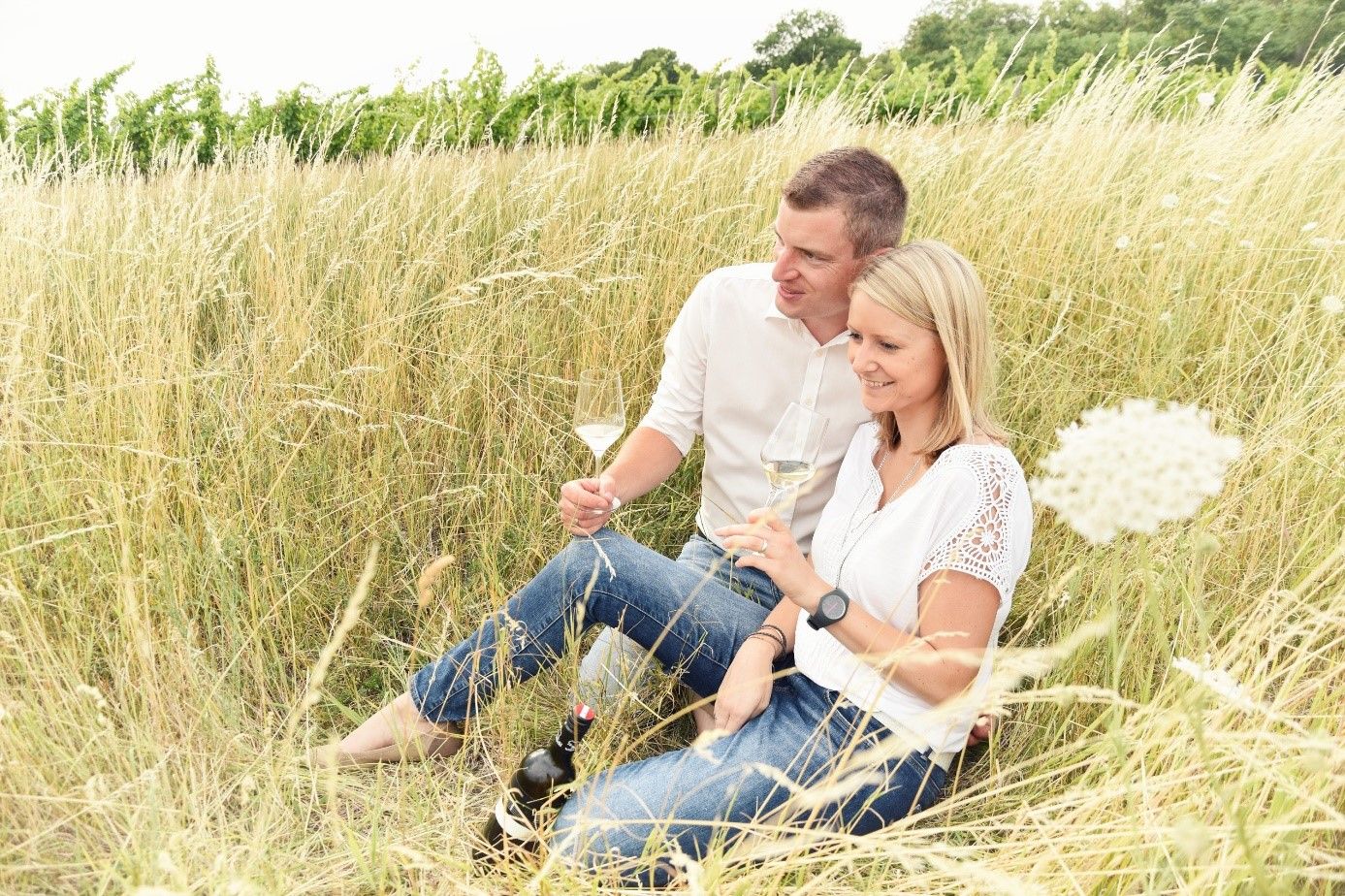 Pár sedí vo vysokej tráve a pije víno.