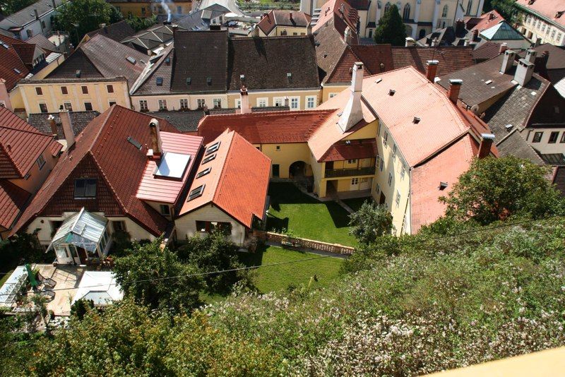 Letecký pohľad na domy s červenými strechami a zeleným vnútorným dvorom.