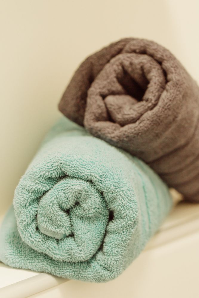 Na poličke ležia dva zrolované uteráky, jeden tyrkysový a druhý hnedý.
