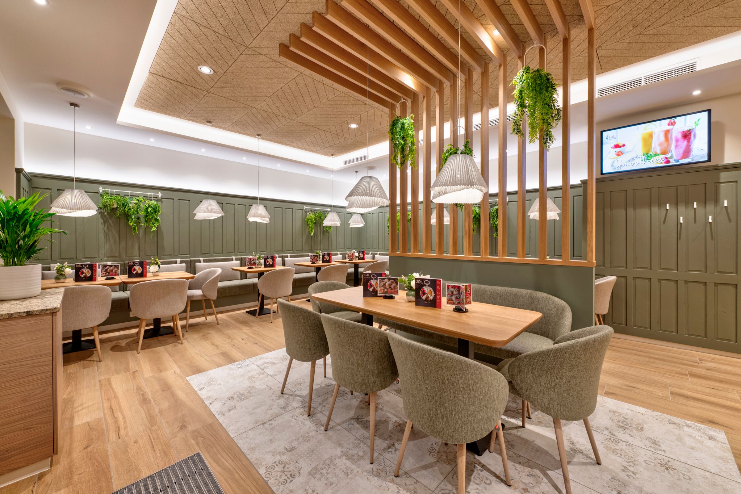 Pohľad do interiéru modernej kaviarne s drevenými stolmi, čalúnenými stoličkami a závesnými rastlinami.