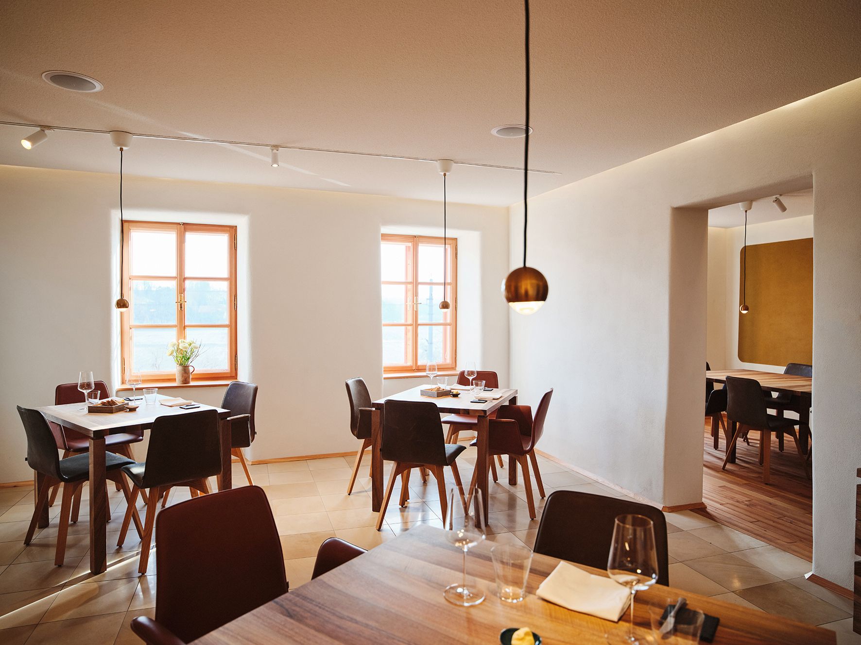 Moderná jedáleň s drevenými stolmi, pohármi na víno a veľkými oknami v minimalistickom dizajne.