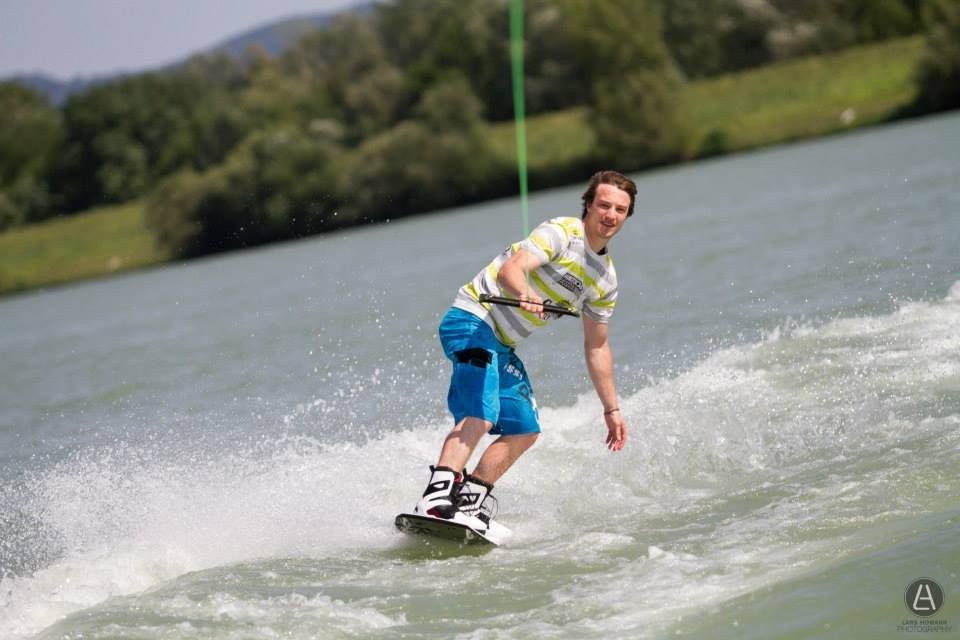 Wakeboardista jazdí na jazere obklopenom zelenou krajinou.