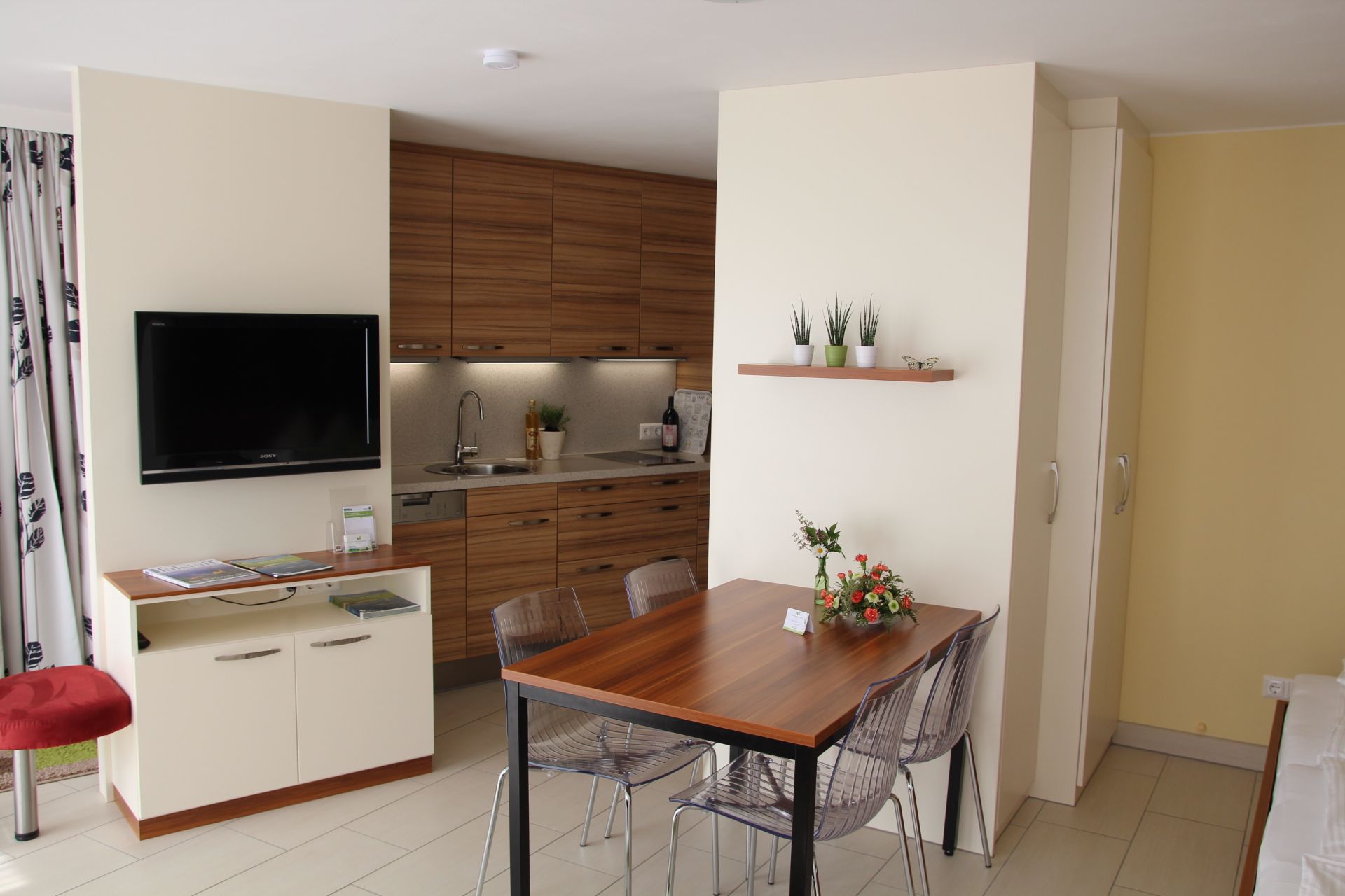 Moderný záhradný byt s kuchyňou, jedálenským stolom a TV.