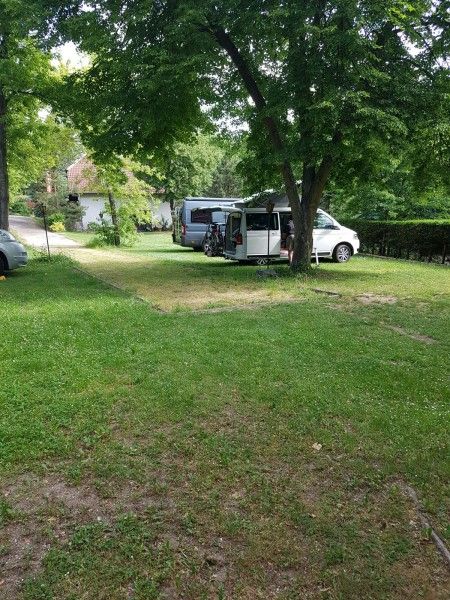 Dva karavany sú zaparkované pod stromami v zelenom kempe.