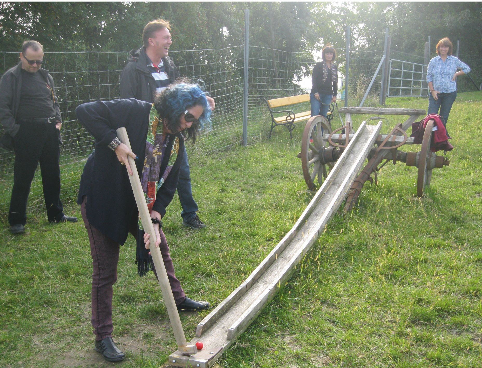 Osoba hrá farmársky golf s drevenou palicou na lúke.
