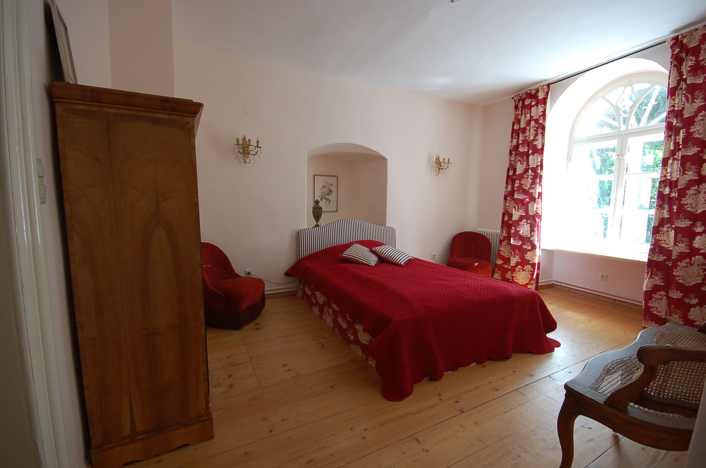 Útulná spálňa s červenou posteľou, červenými závesmi a dreveným nábytkom.