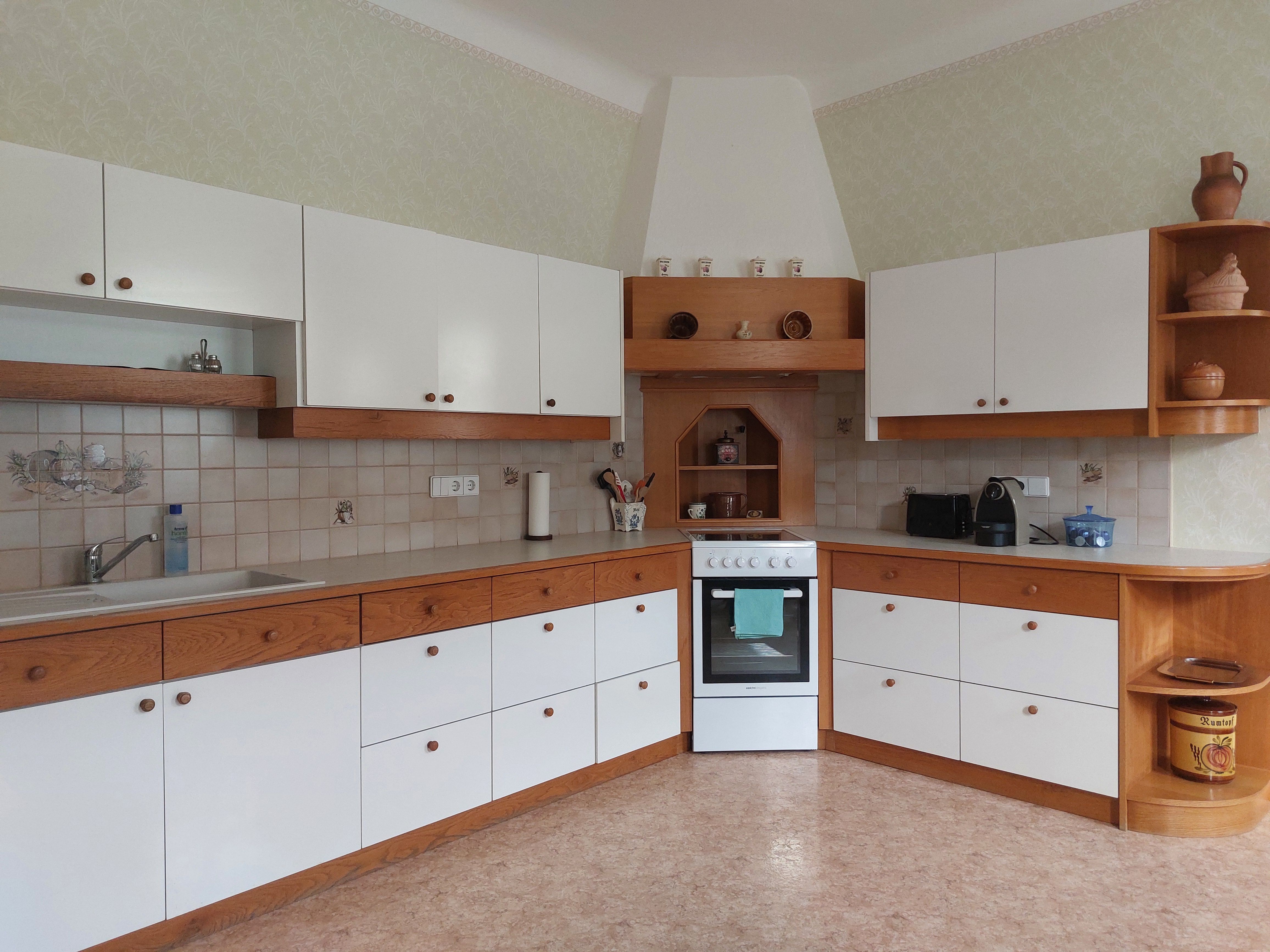 Kuchyňa s bielymi a drevenými skrinkami, sporákom a drezom.