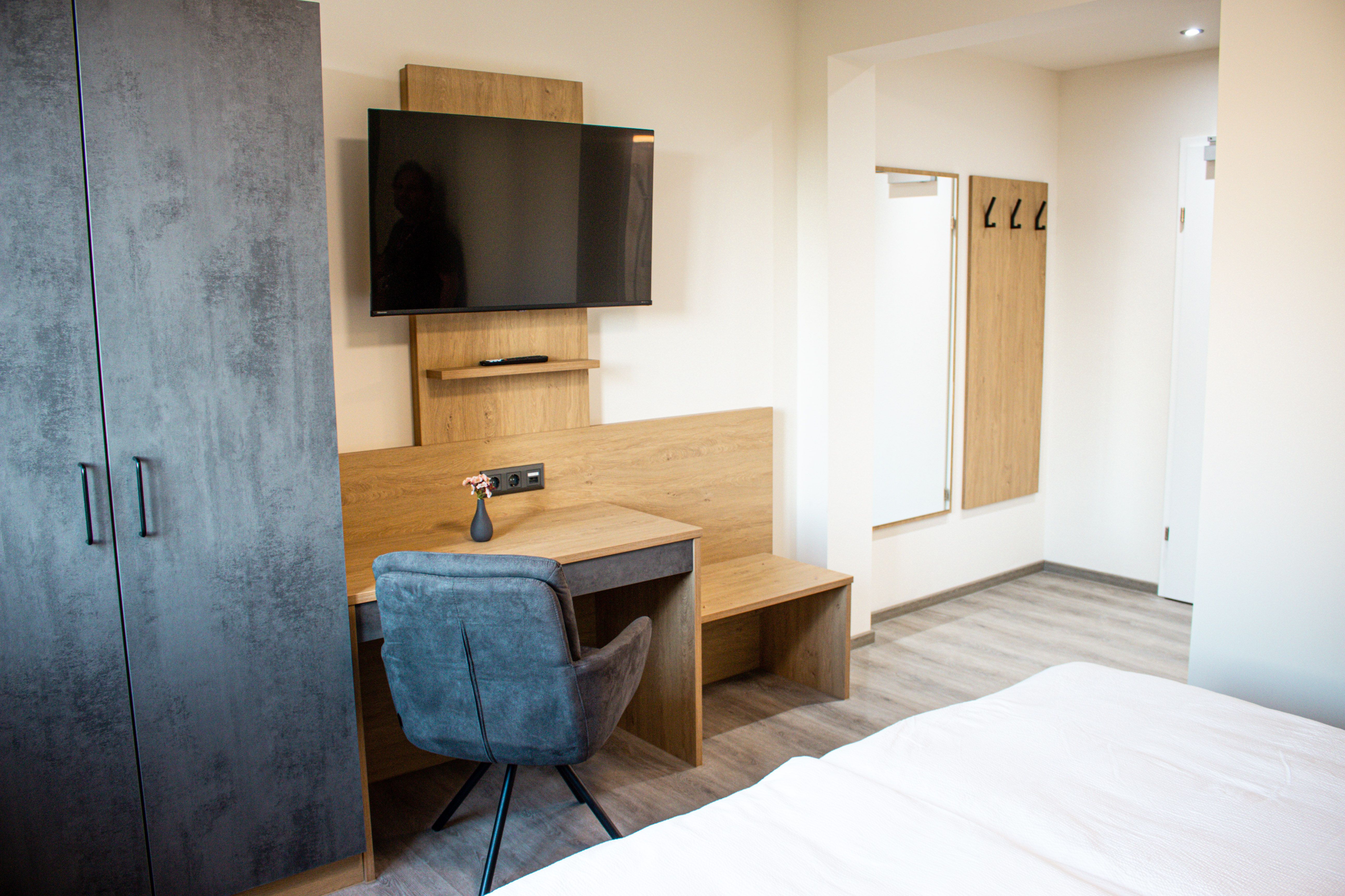 Moderne zariadená hotelová izba so stolom, TV, šatníkom a zrkadlom.