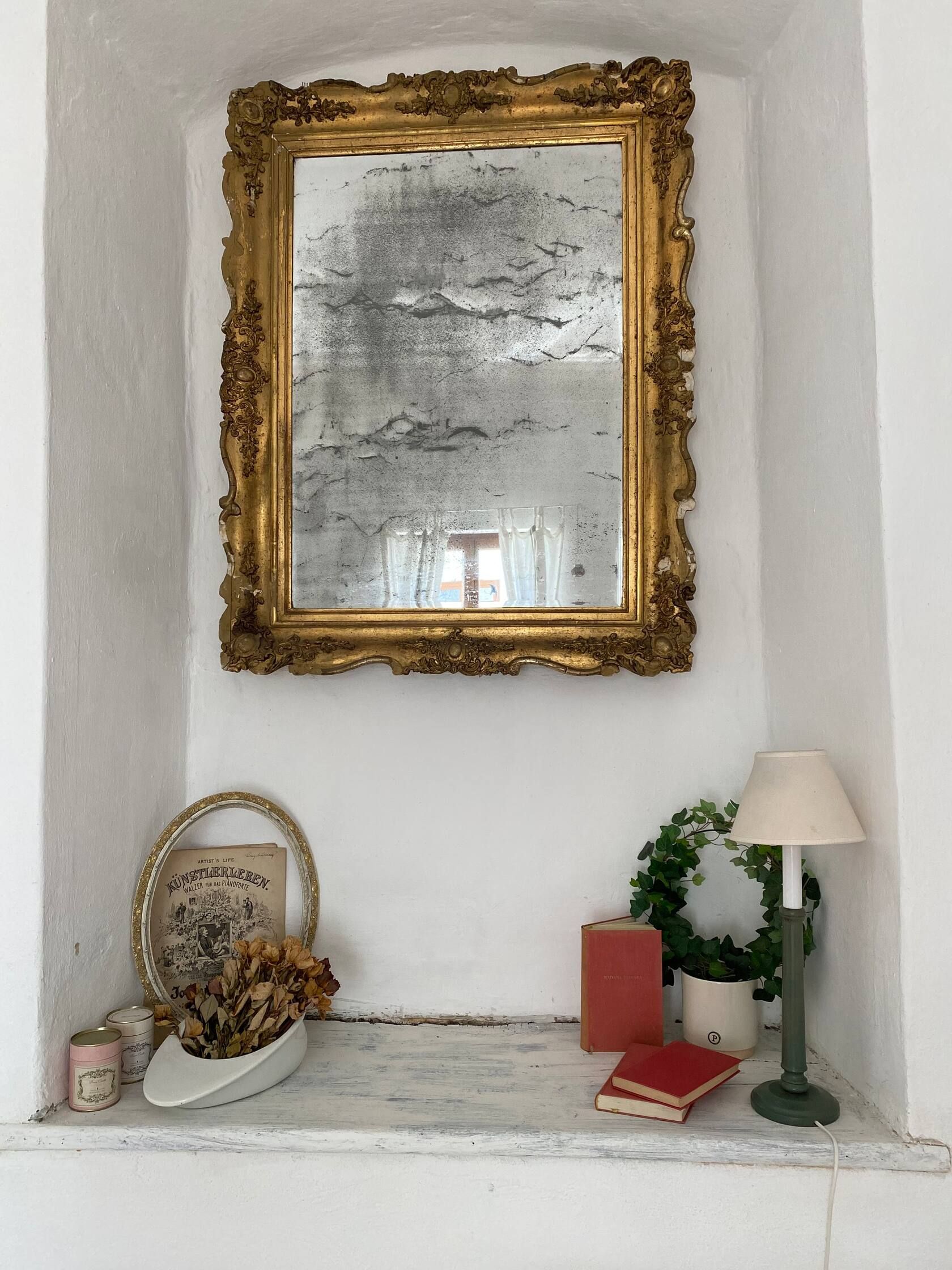 Starožitné zrkadlo so zlatým dekorom nad parapetom s dekoráciou.