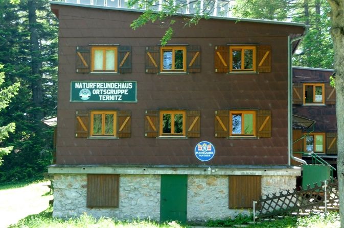 Trojpodlažná budova s drevenými okenicami a nápismi Naturfreunde Ternitz.