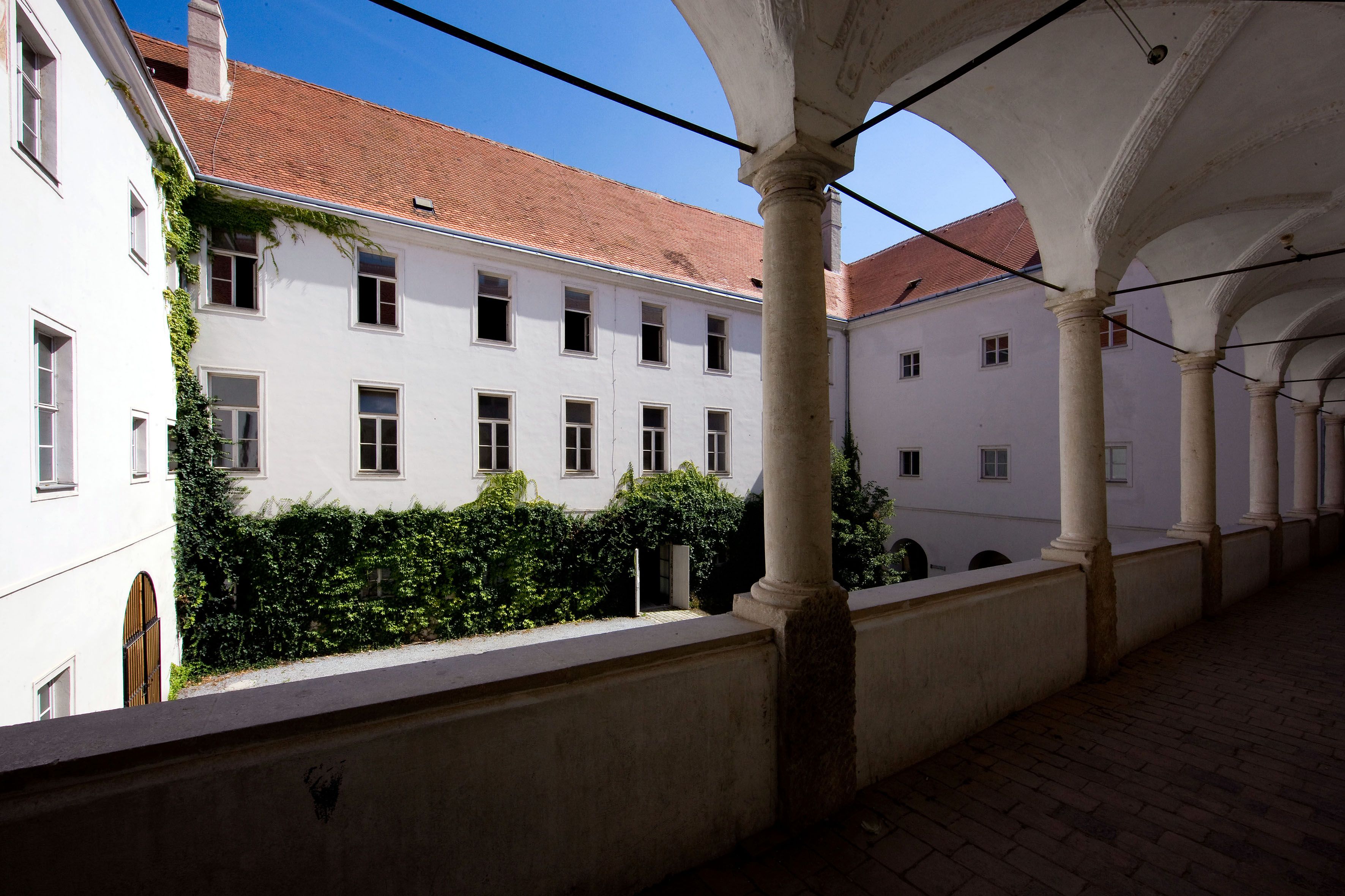 Vnútorné nádvorie historickej budovy s arkádami a múrmi pokrytými brečtanom.