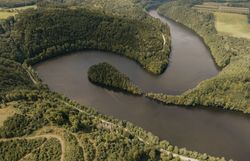Drohnenaufnahme einer breiten Flussschleife mit bewaldeten Ufern im Waldviertel; dunkles Wasser windet sich durch dichtes Grün, Wege und Lichtungen säumen das Ufer.