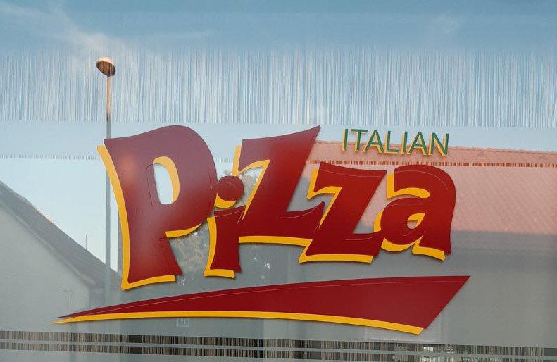 Okenné sklo s veľkým nápisom "Italian Pizza" v červenej a žltej farbe.