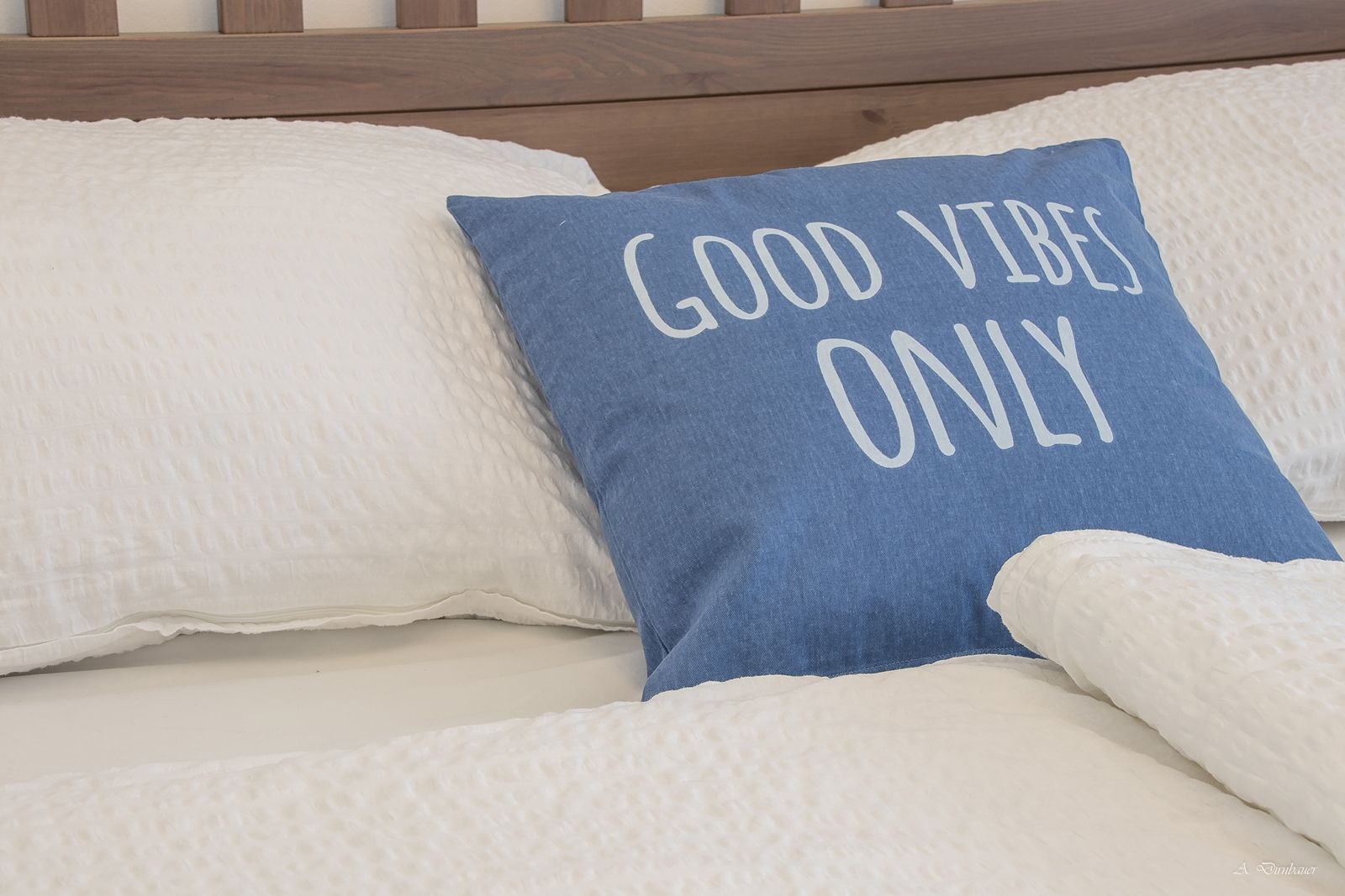 Posteľ s modrým vankúšom s nápisom "Good Vibes Only".