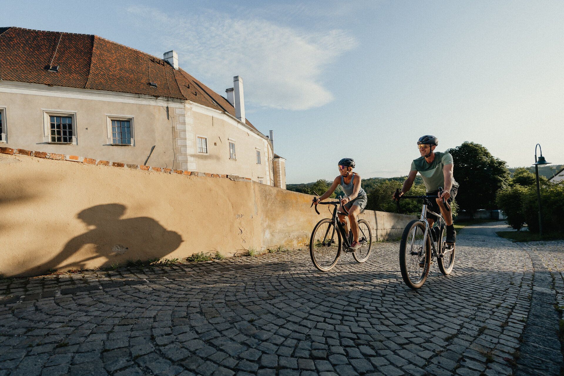 Dvaja cyklisti jazdia po dláždenej ceste pozdĺž starých mestských hradieb v Drosendorfe.