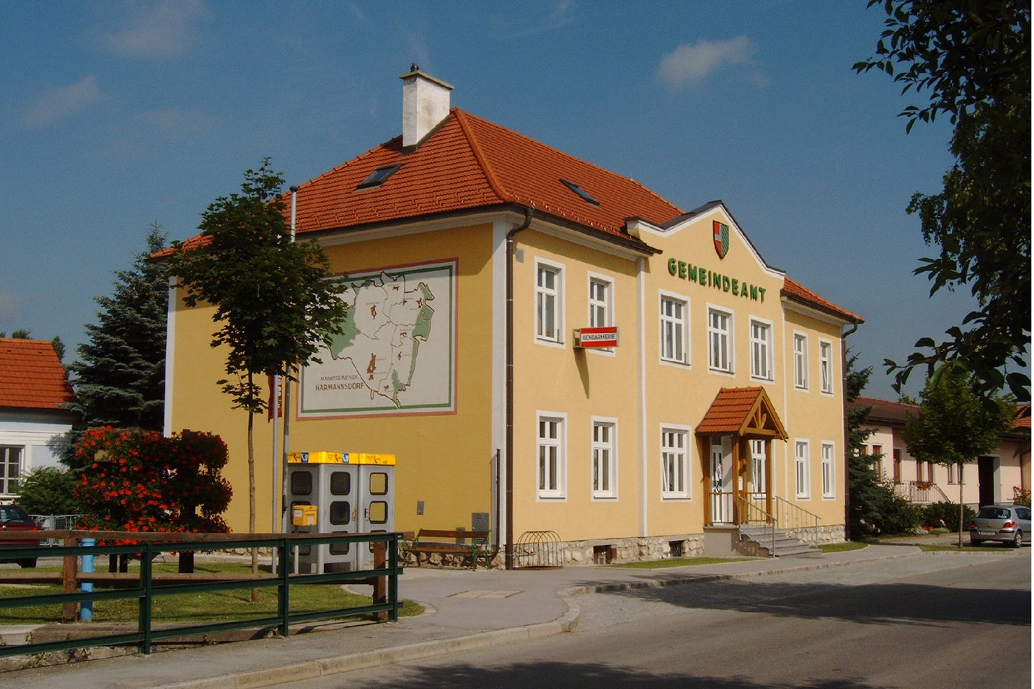 Žltá budova s nápisom "Gemeindeamt", erbom a mapou na stene.