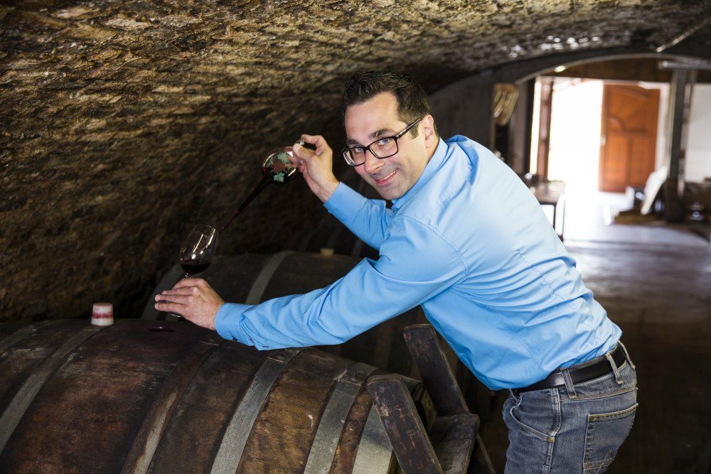 Muž v modrej košeli čerpá víno zo suda vo vínnej pivnici.