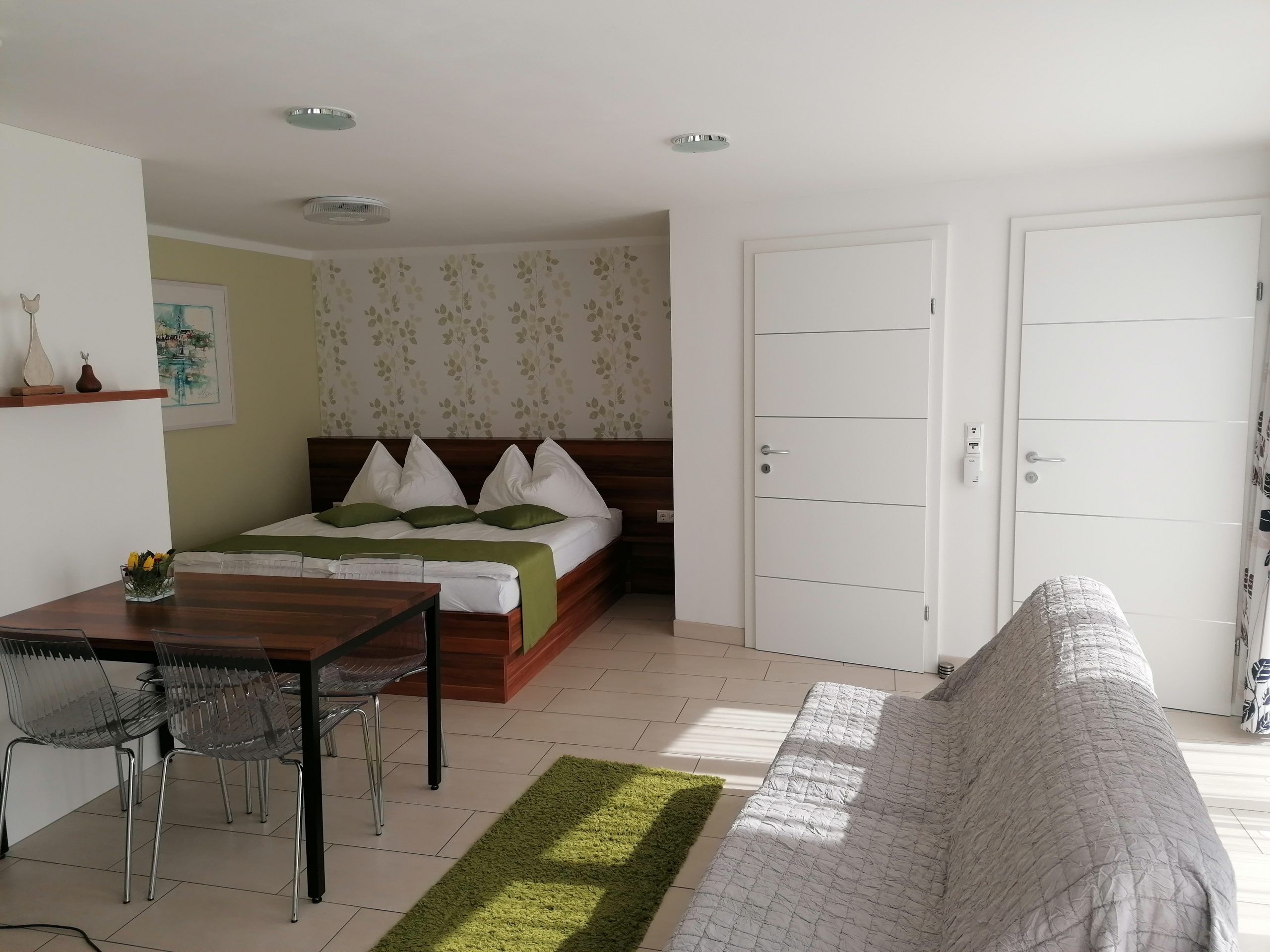 Izba s manželskou posteľou a dvoma bielymi vchodovými dverami