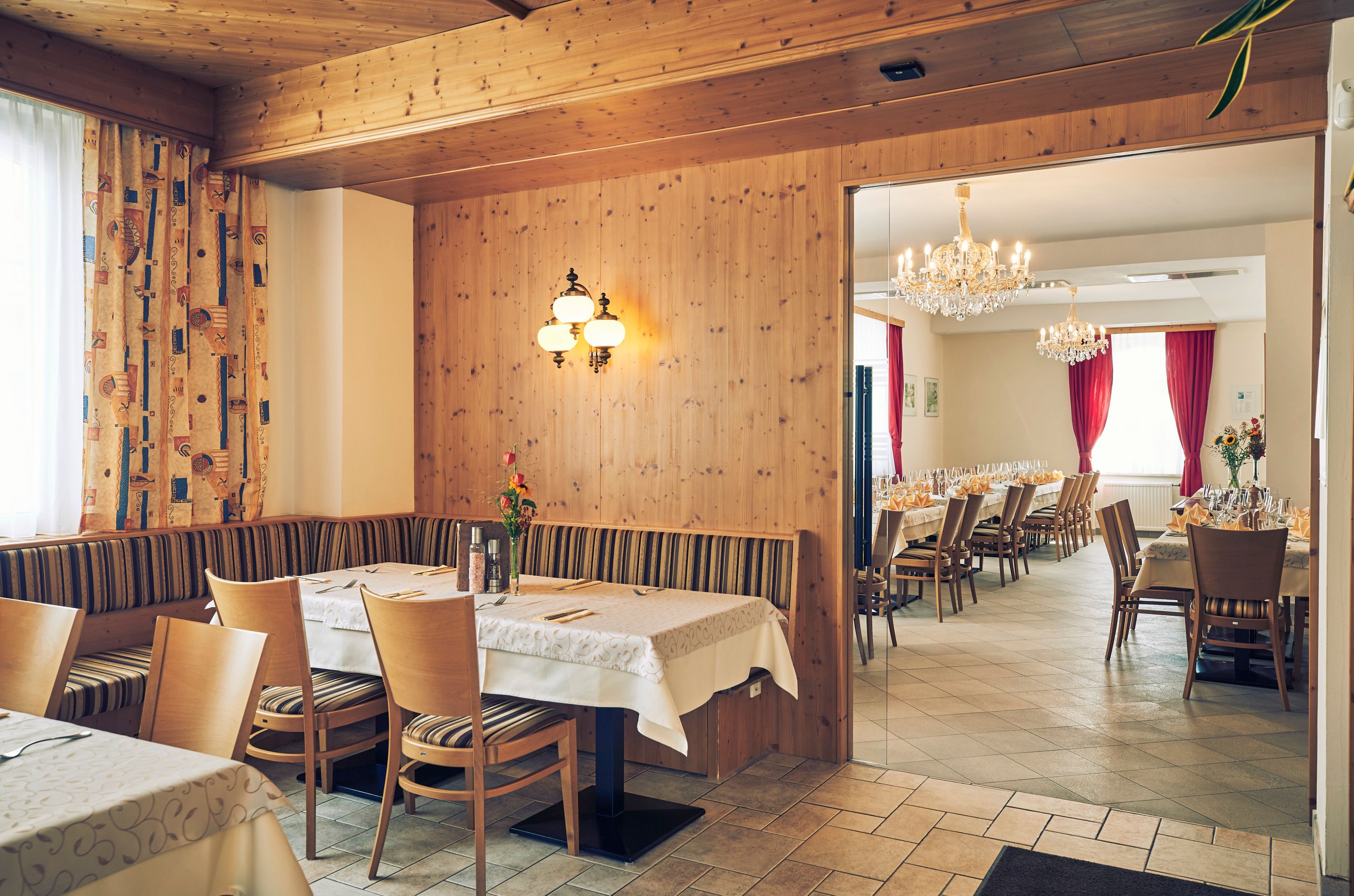 Útulná hosťovská izba s drevenými stenami a priľahlou banketovou sálou s lustrami a prestretými stolmi.