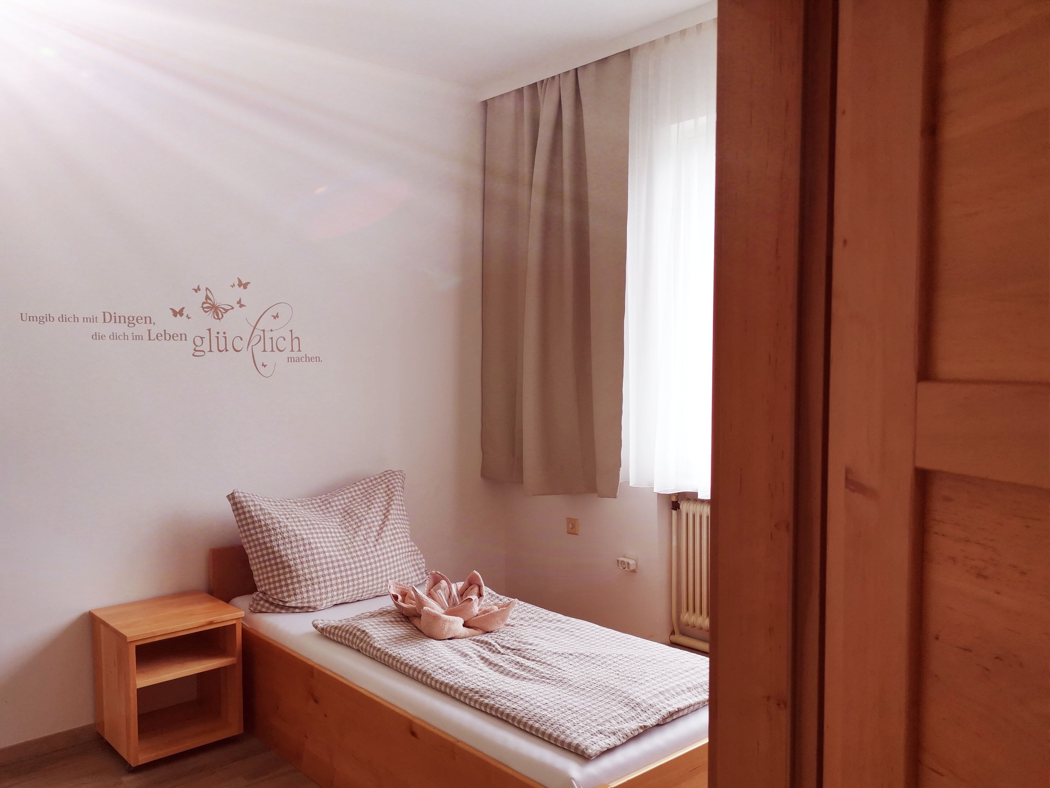 Jednoduchá izba pre hostí s jednou posteľou, drevenými policami a citátom na stene.