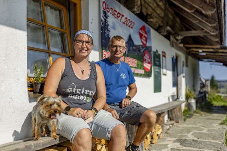 Dvaja ľudia sedia pred budovou so psom, v pozadí plagát s dátumom 09. septembra 2023.