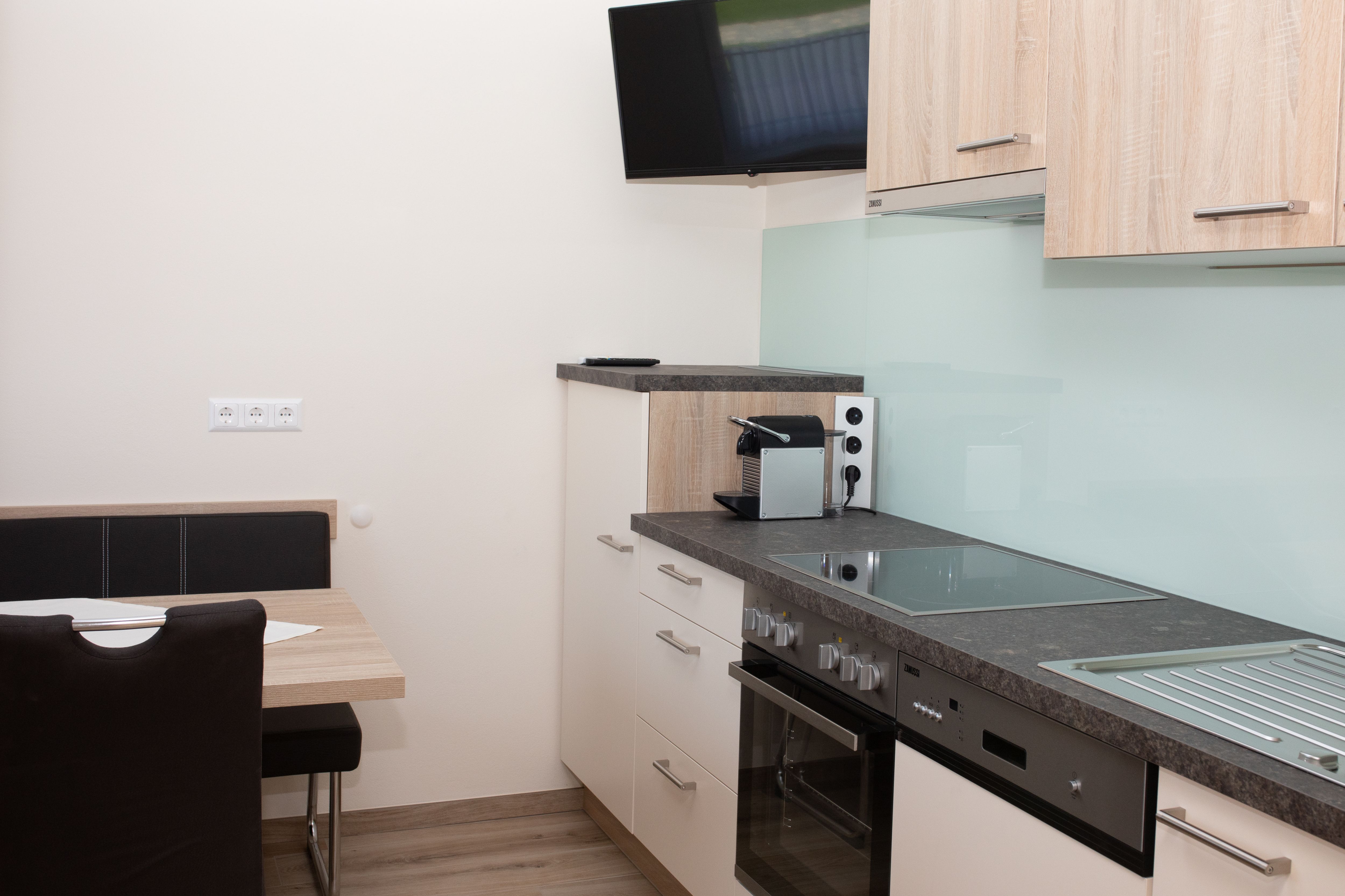 Moderná kuchyňa so sporákom, drezom, kávovarom a nástenným TV.