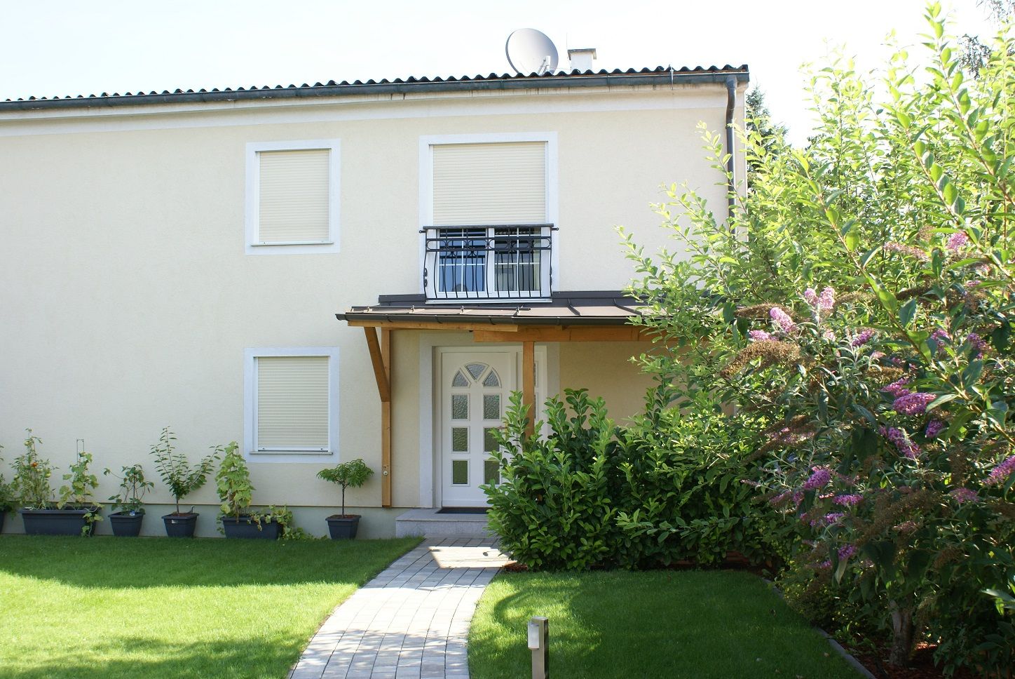 Exteriérový pohľad na dvojpodlažný dom so záhradou a rastlinami.