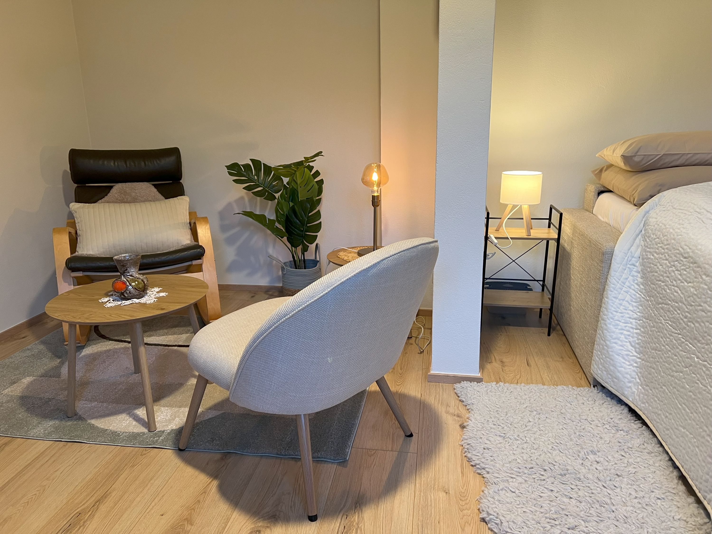 Útulná spálňa s kreslom, stolom, rastlinou a posteľou.