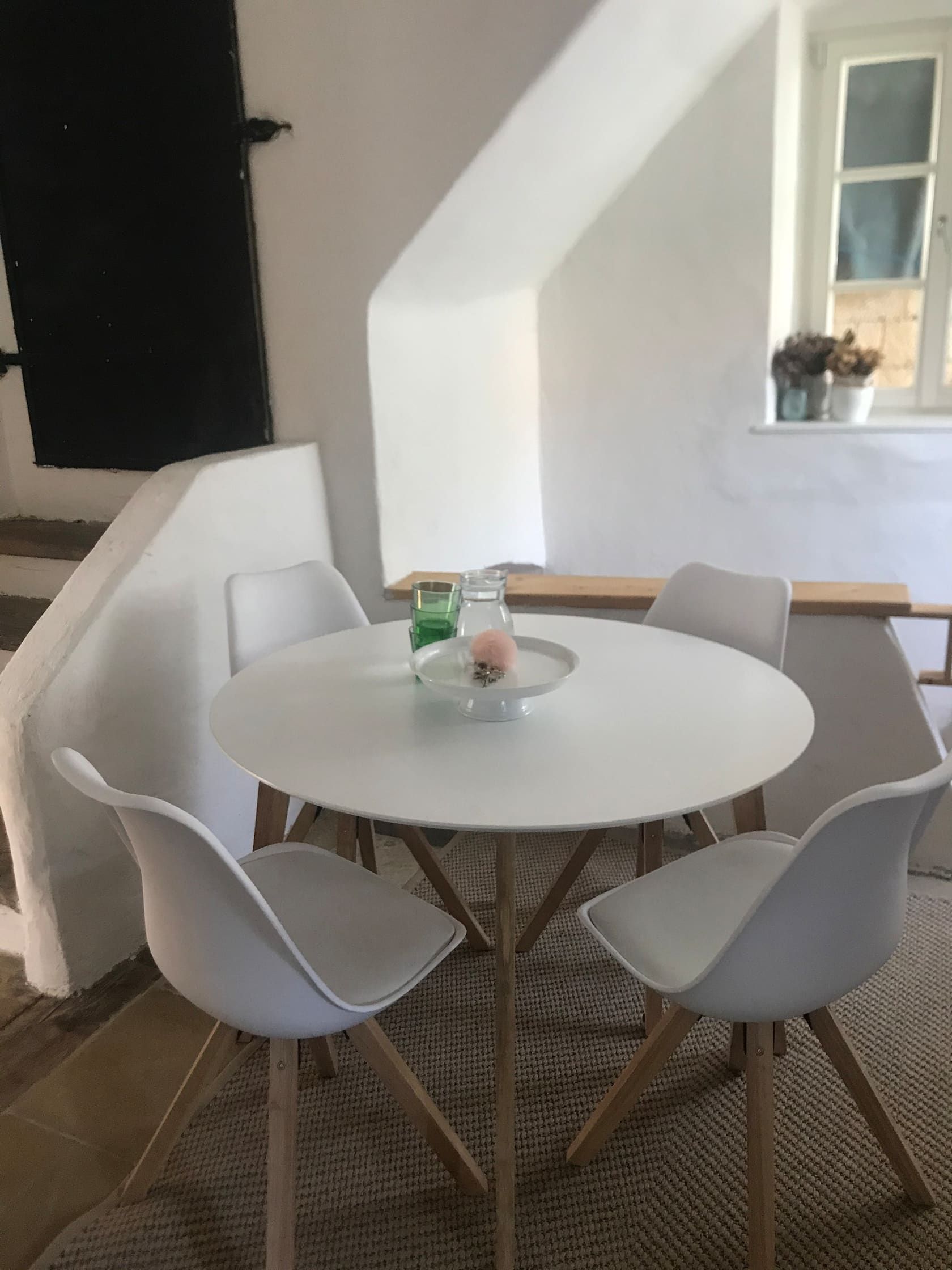 Moderné posedenie s okrúhlym stolom a štyrmi bielymi stoličkami v presvetlenej miestnosti.