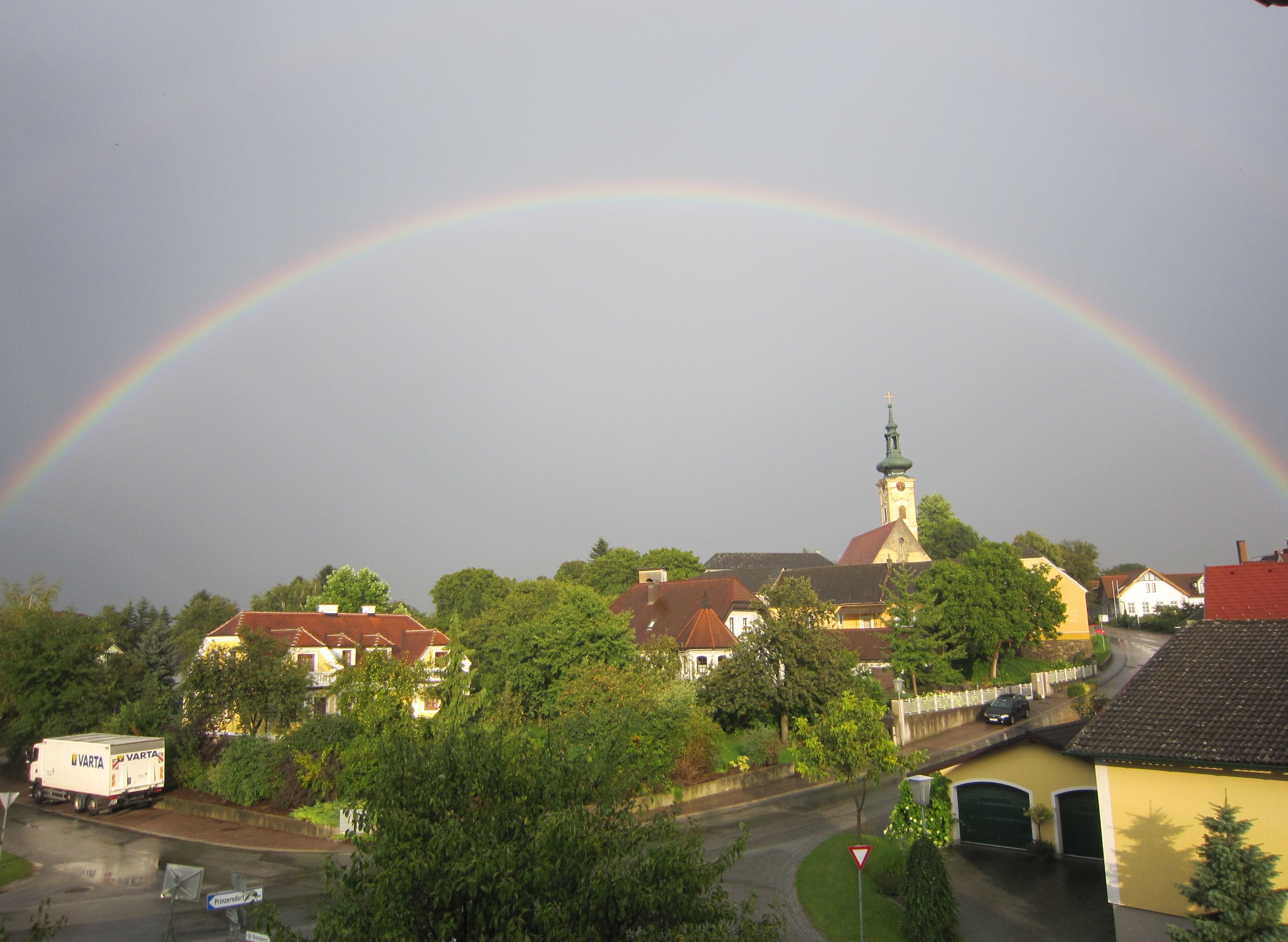 Dúha sa tiahne nad dedinou s kostolom a domami v Gerersdorfe.