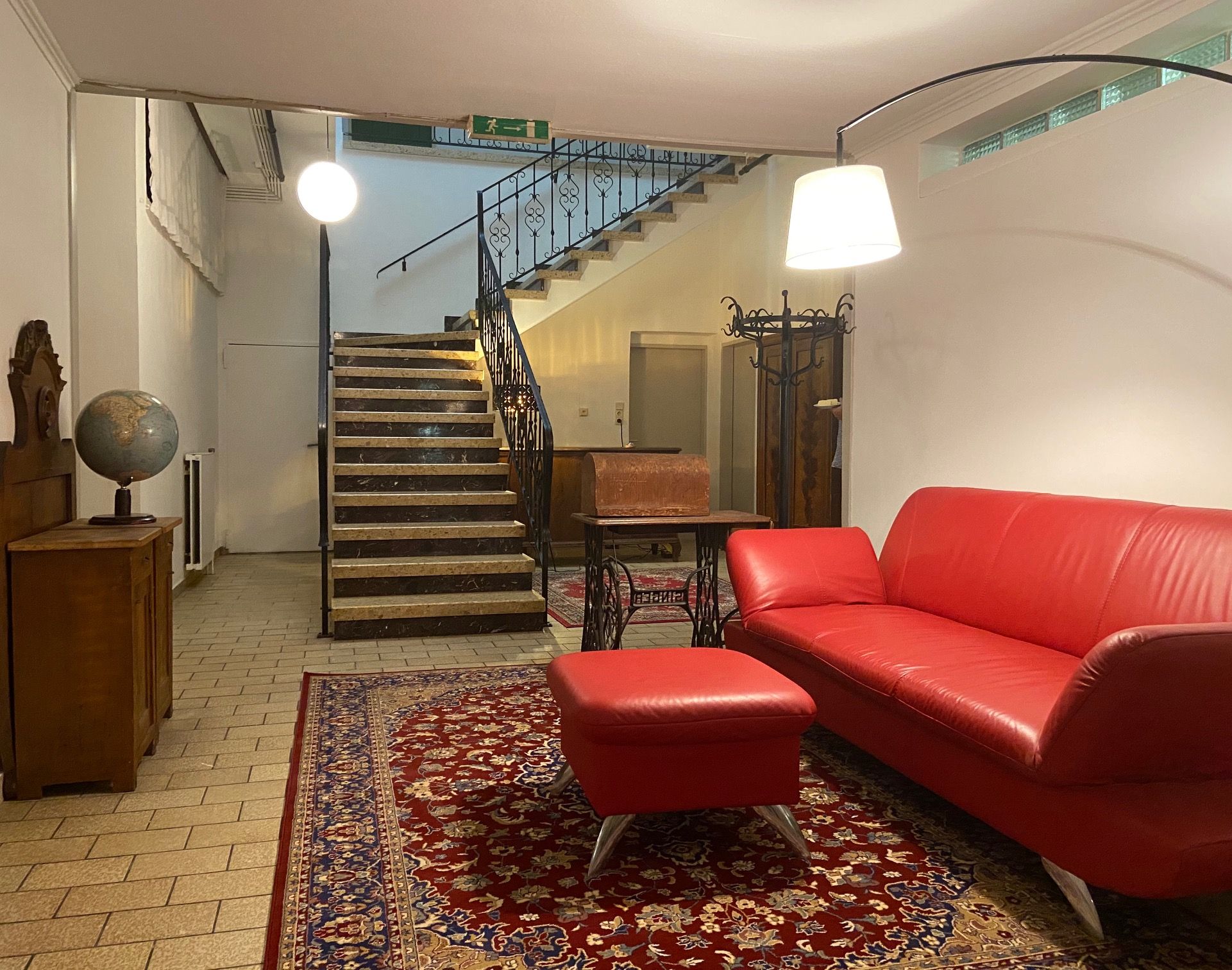 Foyer s červenou pohovkou, kobercom, glóbusom a schodiskom.