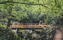 Ein malerischer Wanderweg schlängelt sich durch die üppige, grüne Landschaft, umgeben von rauschenden Wasserfällen und sanften Hügeln. Die frische, klare Luft und das sanfte Plätschern des Wassers laden dazu ein, die Natur in vollen Zügen zu genießen und die Seele baumeln zu lassen.