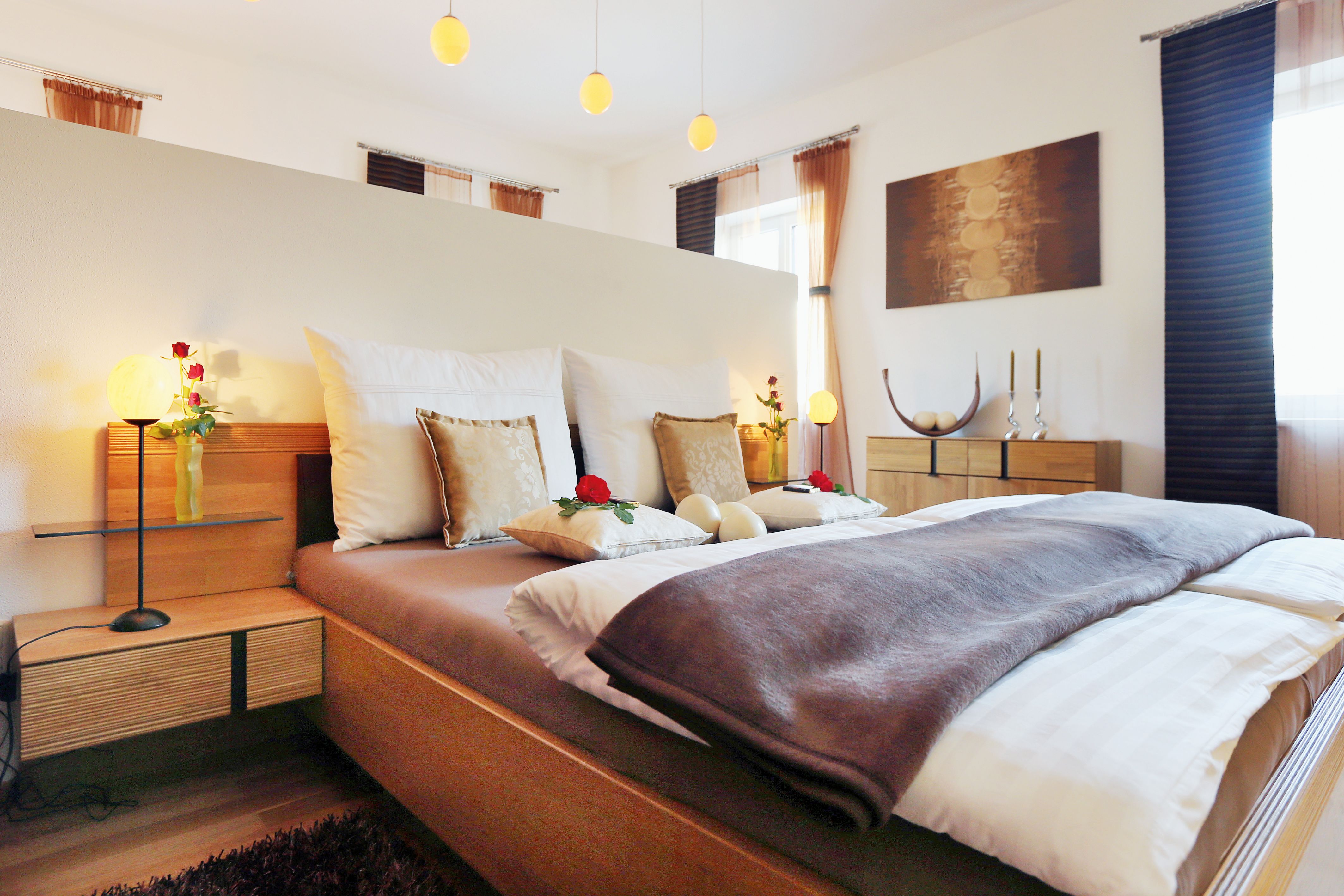 Útulná spálňa s manželskou posteľou, zdobená vankúšmi a ružami, dreveným nábytkom a mäkkým osvetlením.