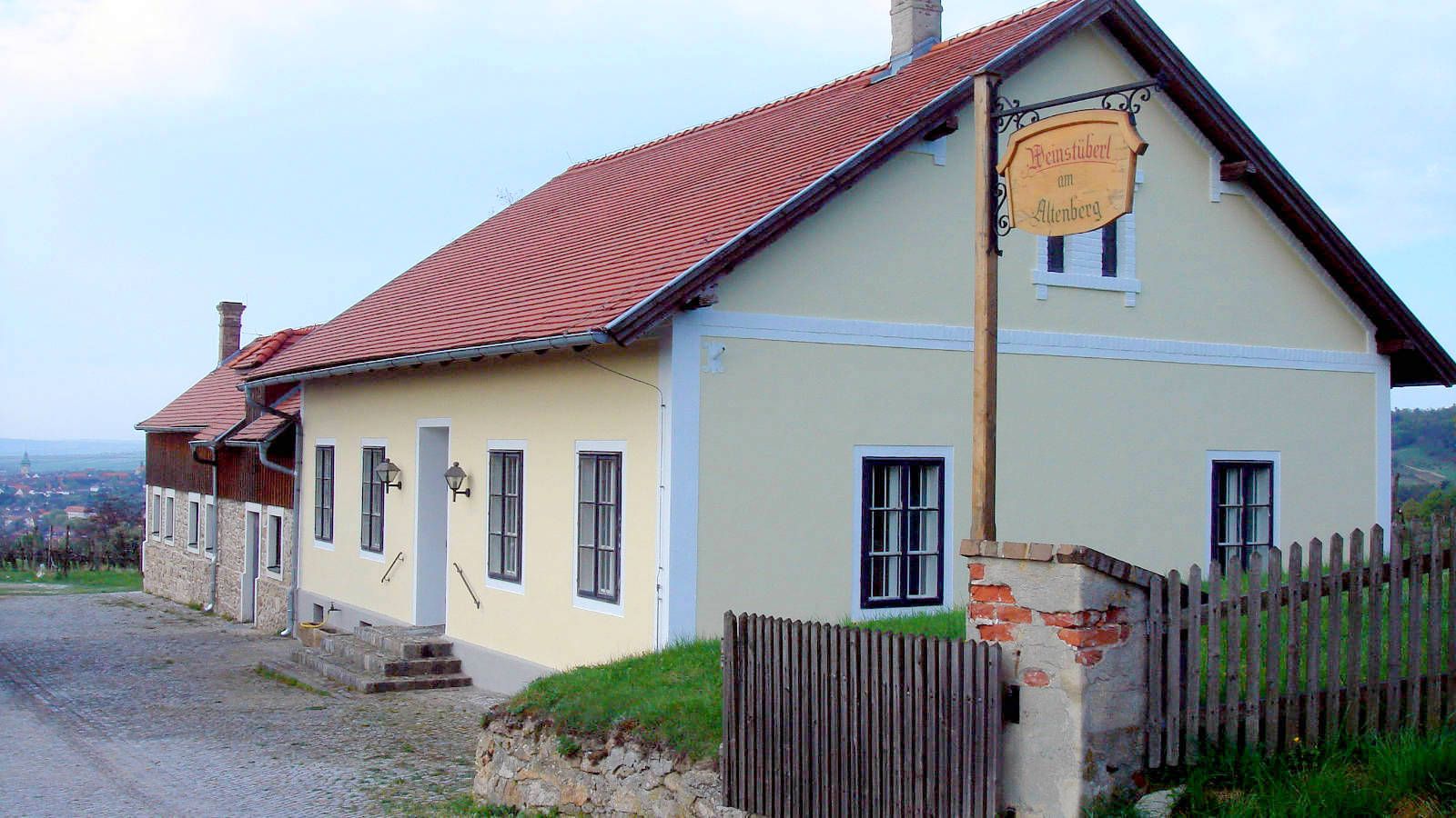 Vinohradnícky dom so žltou fasádou a červenou strechou vo vidieckom prostredí.