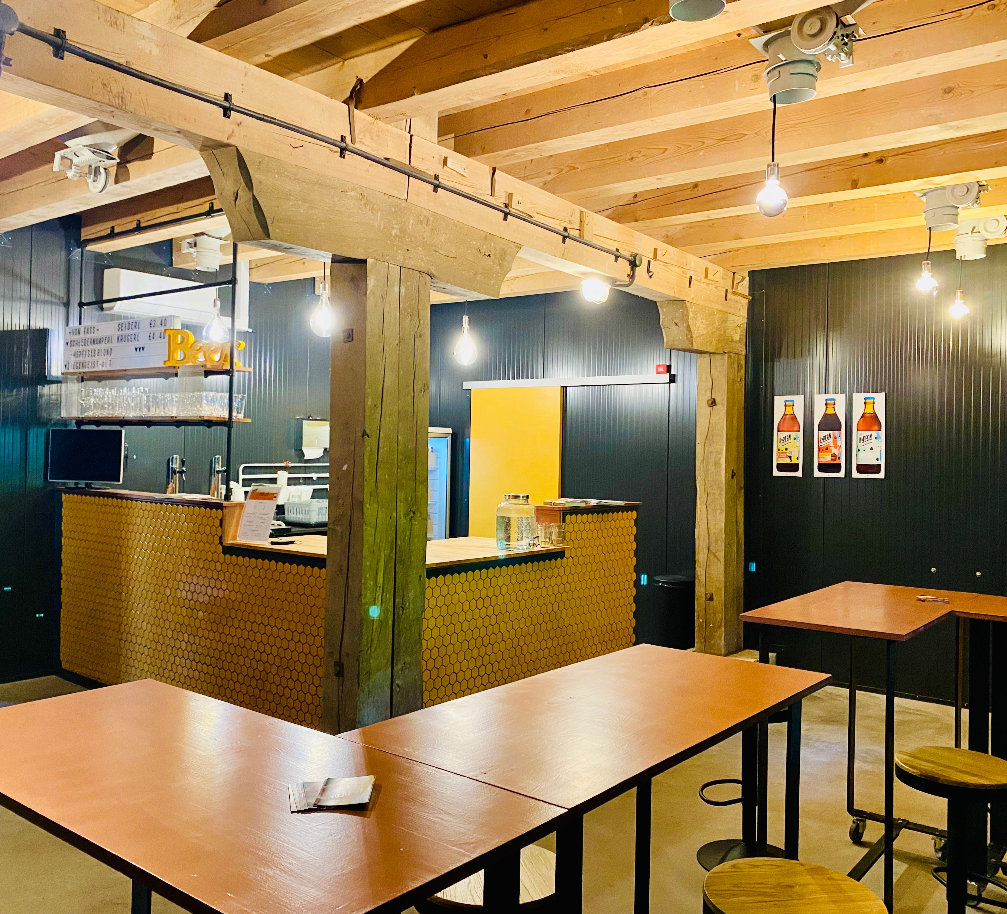 Pohľad do interiéru modernej kaviarne s drevenými trámami, barovým pultom a vysokými stolmi.