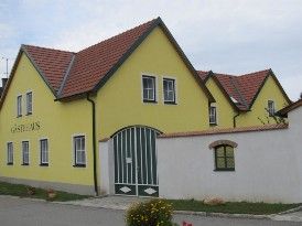 Žltá budova s červenou strechou a zelenou bránou, označená ako "Guest House".