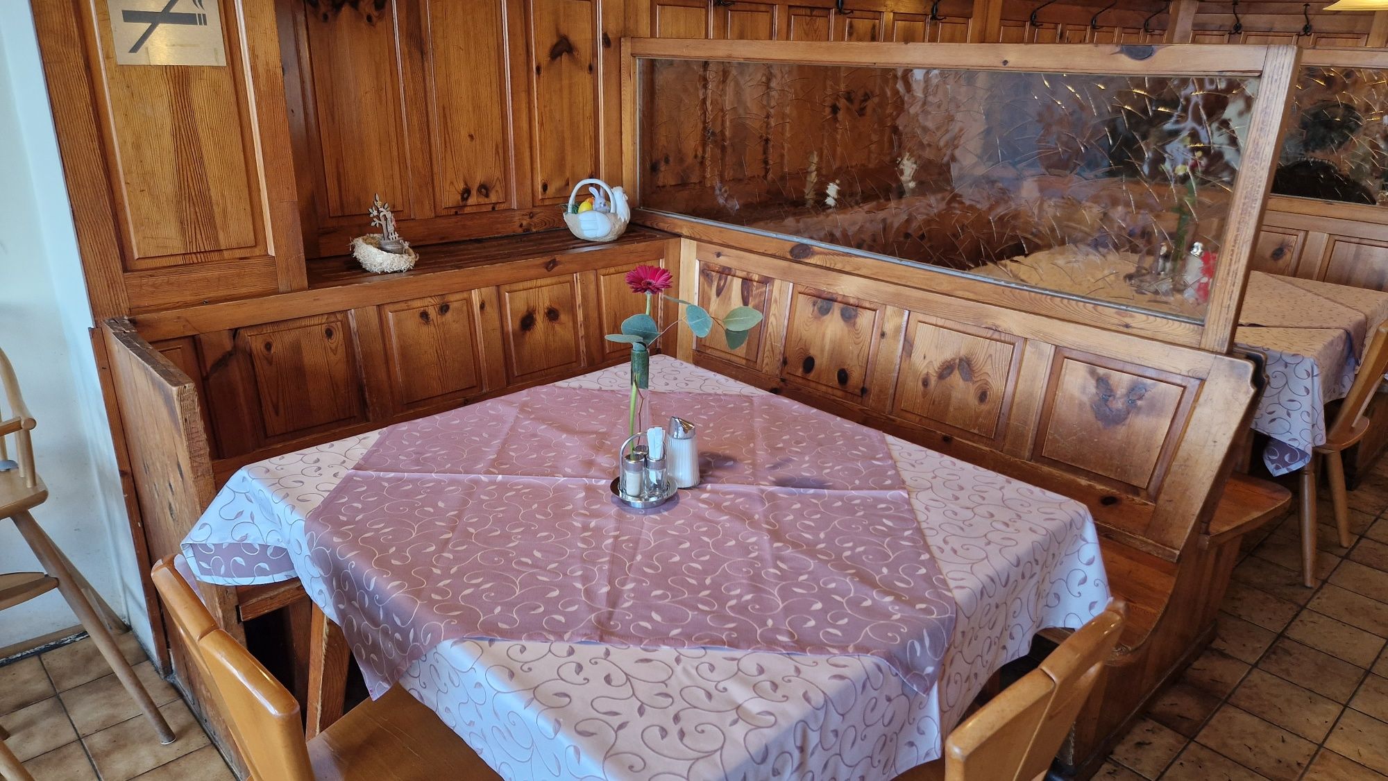 Útulný stôl v rustikálnej izbe pre hostí s dreveným obložením, obrusom a vázou s kvetom.
