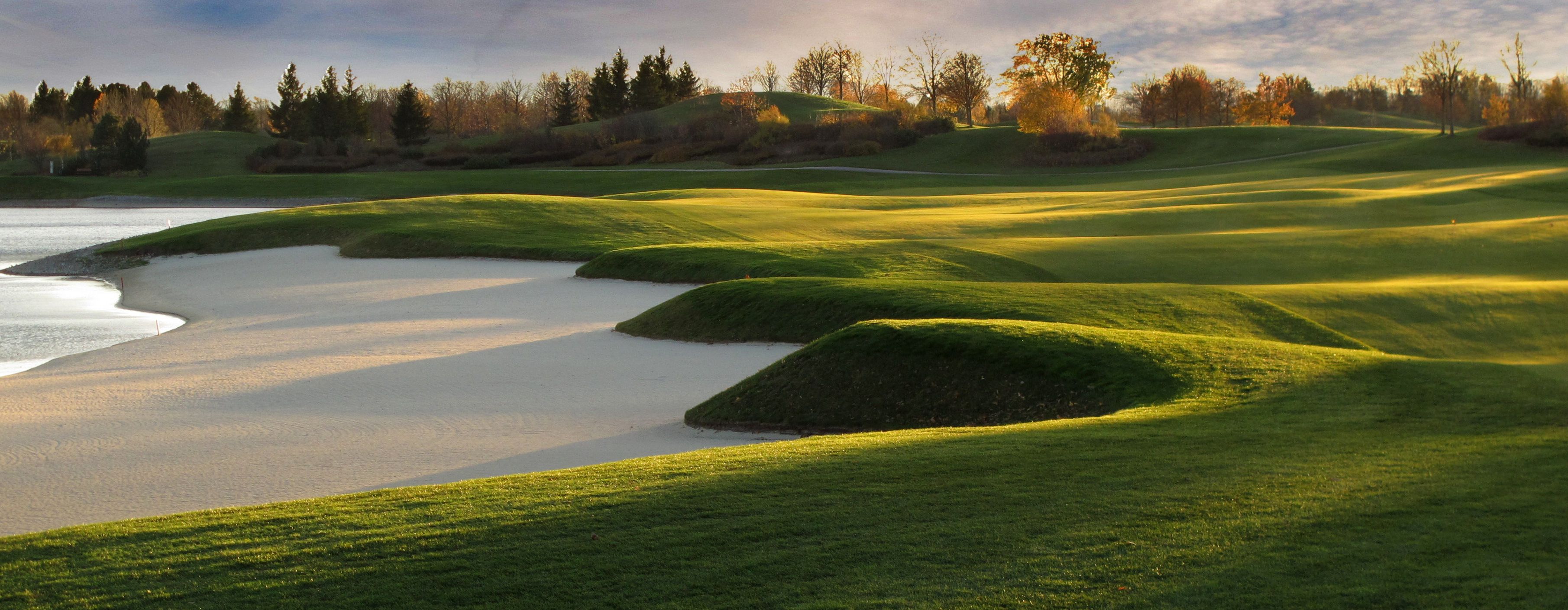 Panoráma golfového ihriska s pieskovými bunkrami a zelenými kopcami v slnečnom svetle.