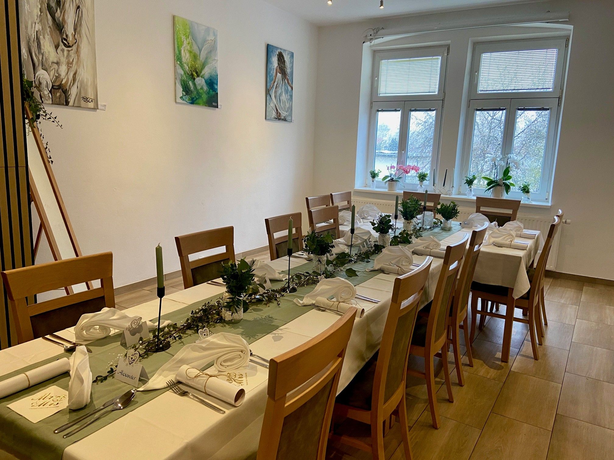 Sviatočne prestretý stôl v miestnosti s umeleckými dielami na stenách a veľkými oknami.