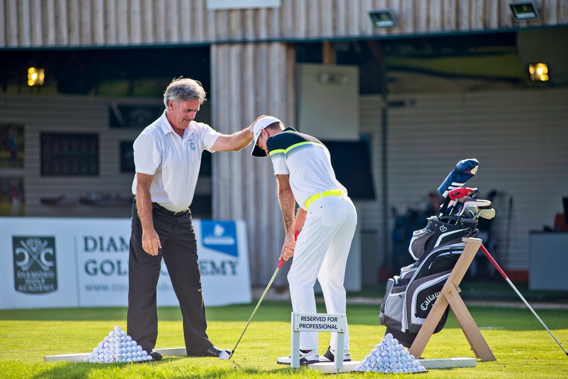 Golfový inštruktor dáva pokyny študentovi na tréningovom ihrisku v Diamond Golf Academy.