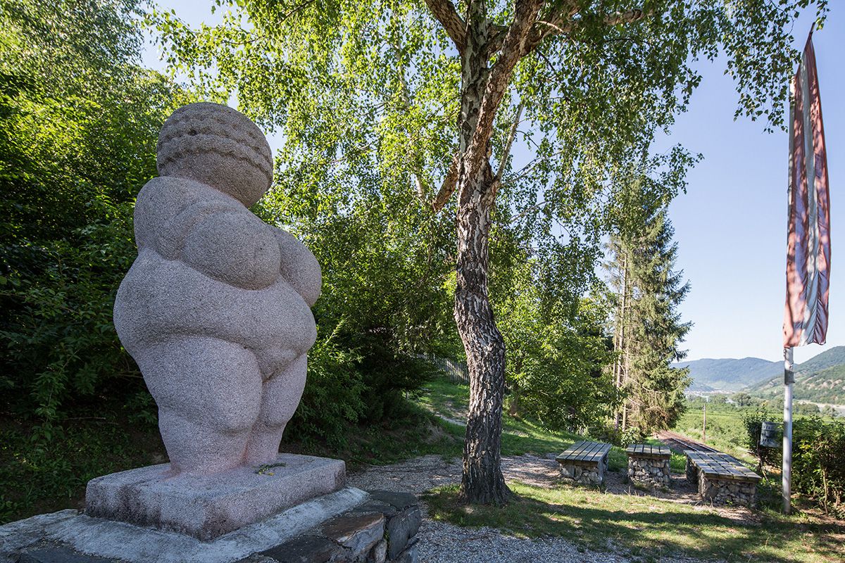 Venuša na podstavci v pozadí strom a lavičky