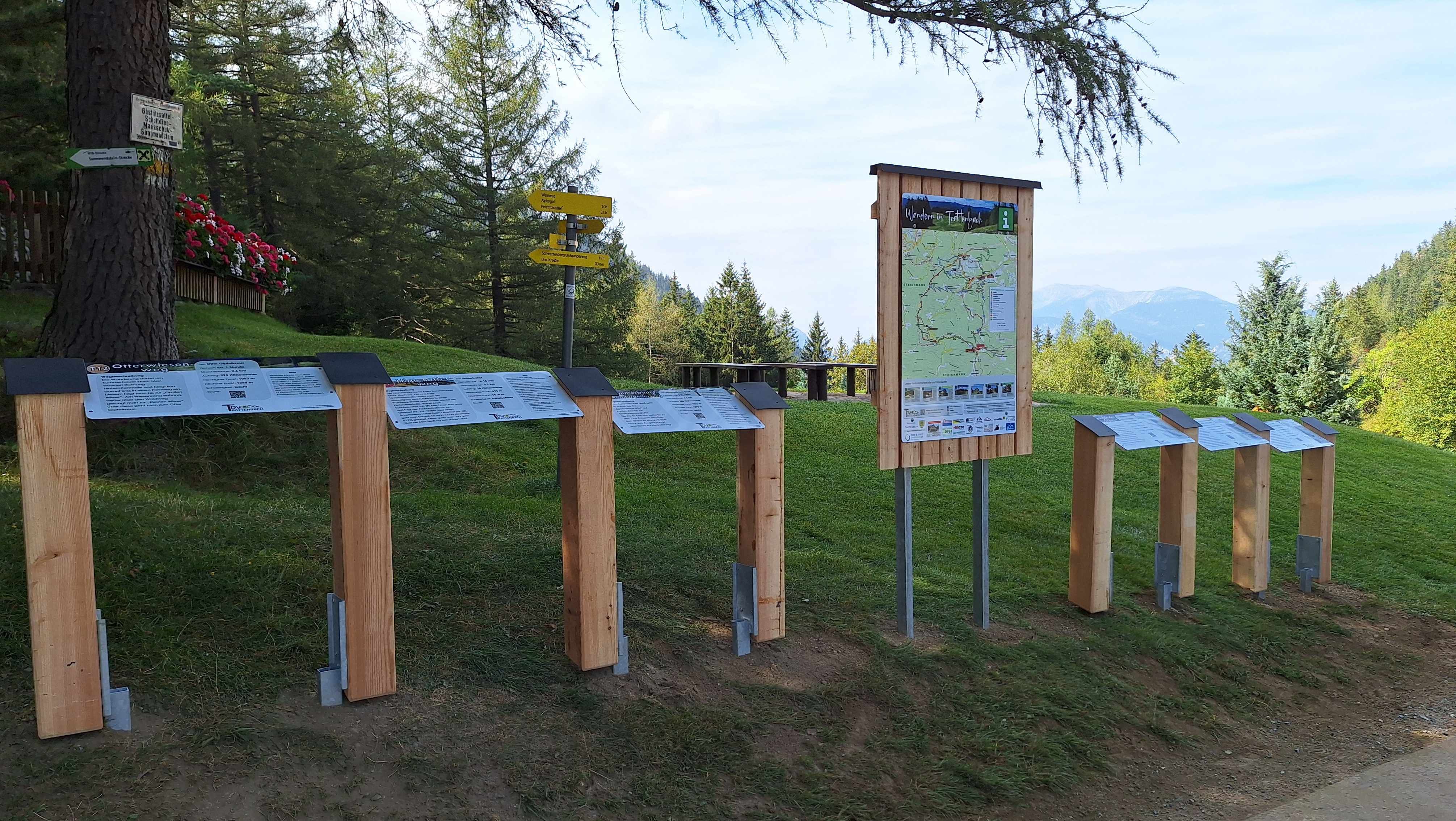 Turistické smerovníky a informačné tabule v zelenej horskej krajine.