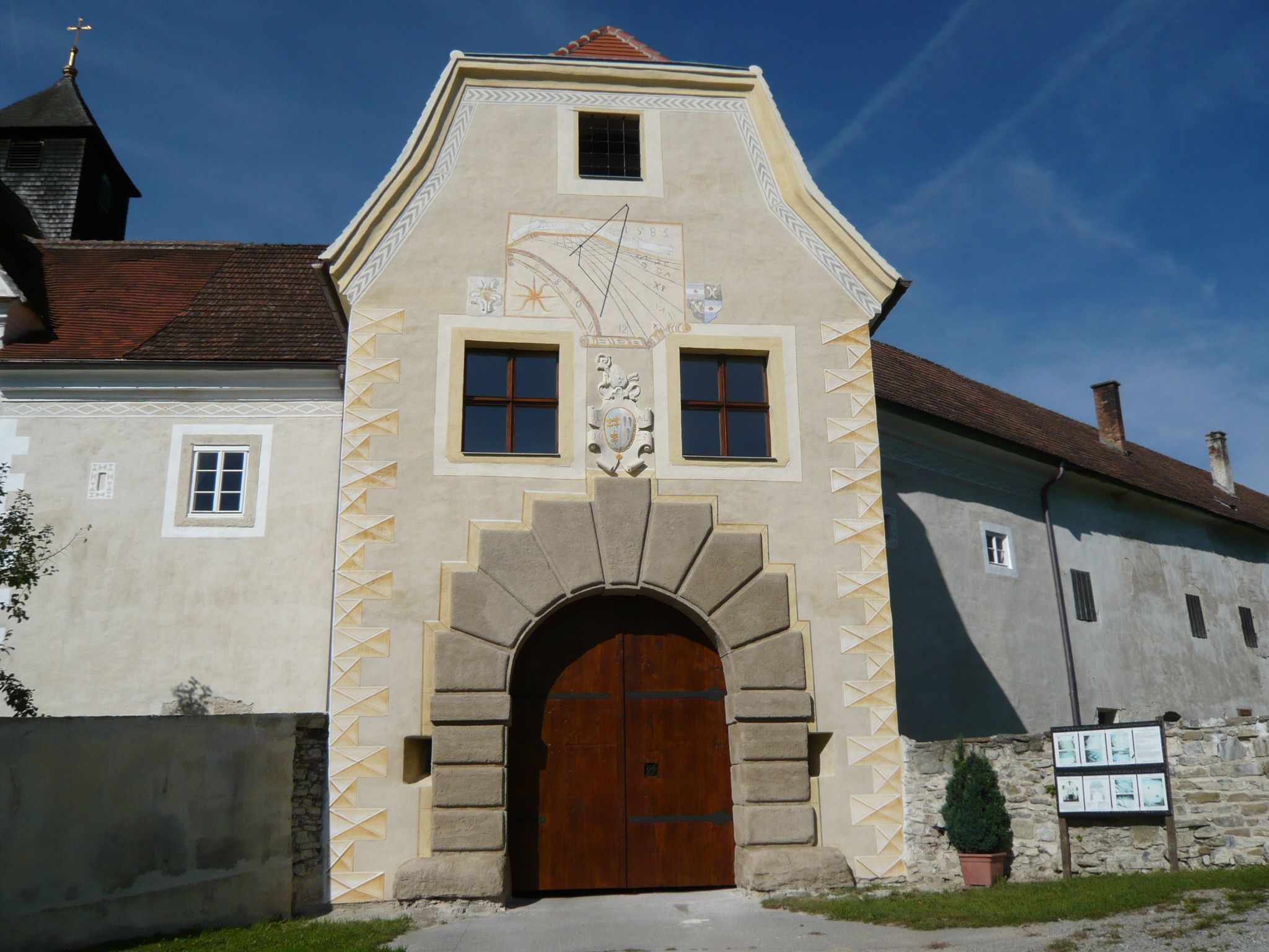 Vstupná brána do hradu Kreisbach so slnečnými hodinami a erbom.