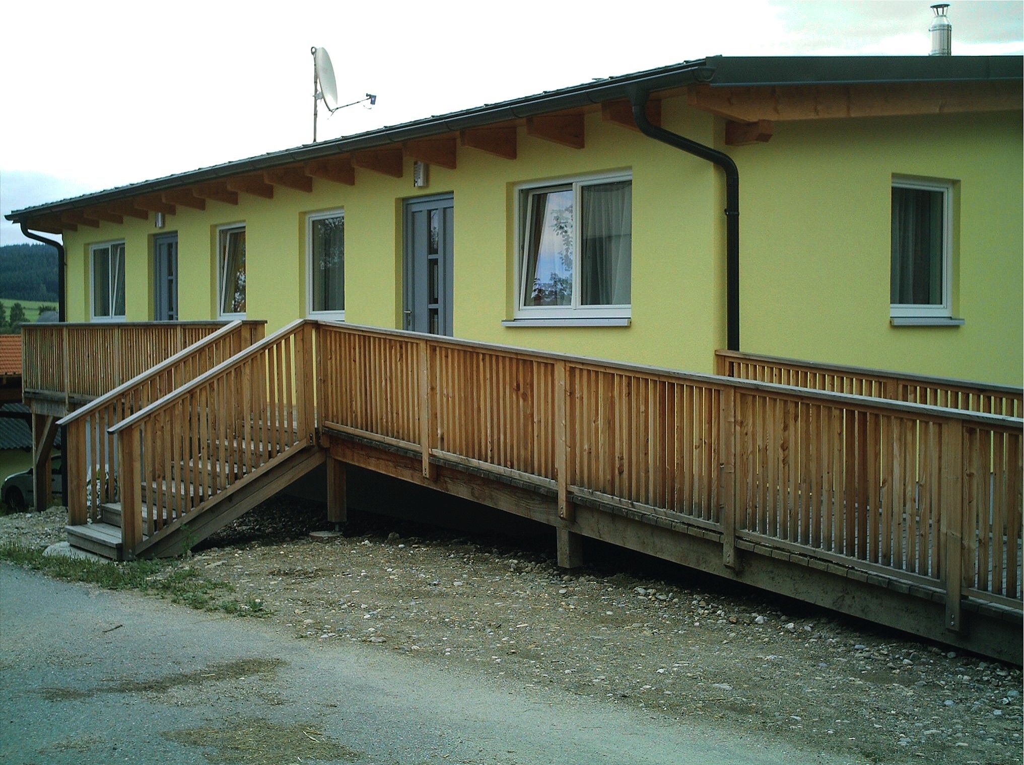 Žltá budova s drevenou rampou a oknami.
