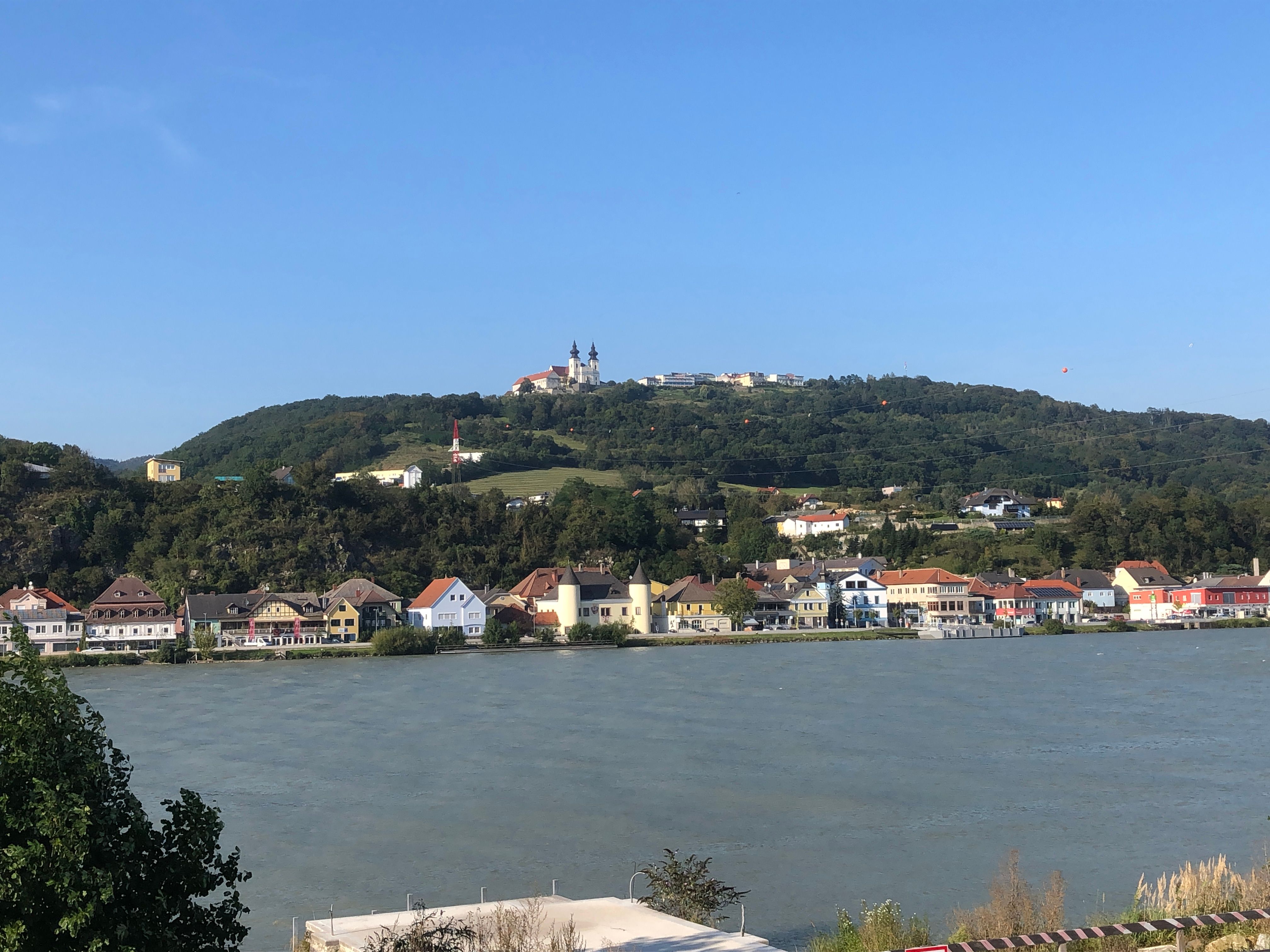 Pohľad na baziliku Márie Taferl na kopci s domami a riekou v popredí.