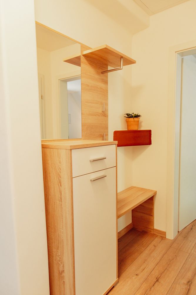 Moderná predsieň s drevenou skriňou, zrkadlom a rastlinou.