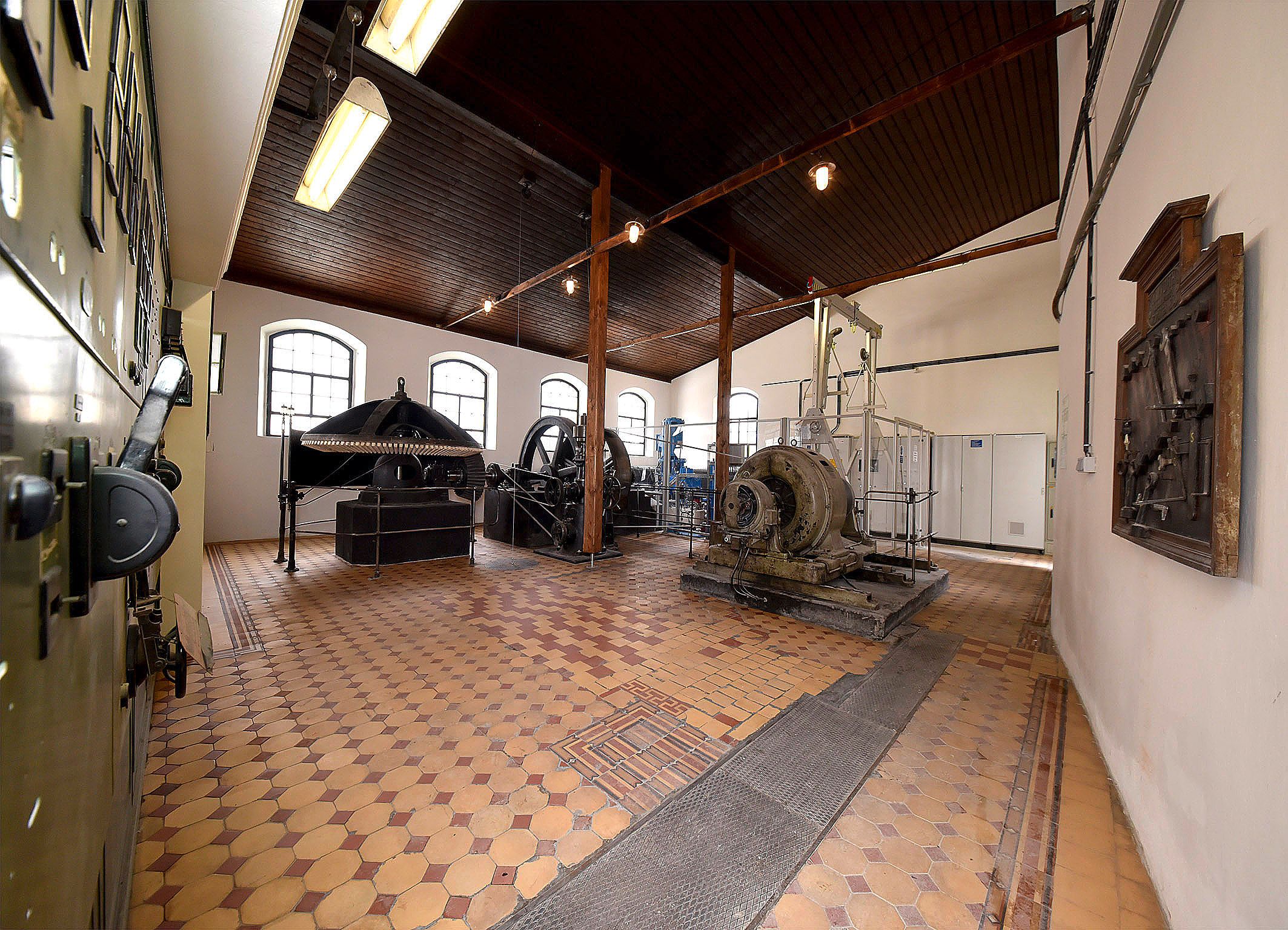 Pohľad do interiéru historickej elektrárne so strojmi a zariadeniami.